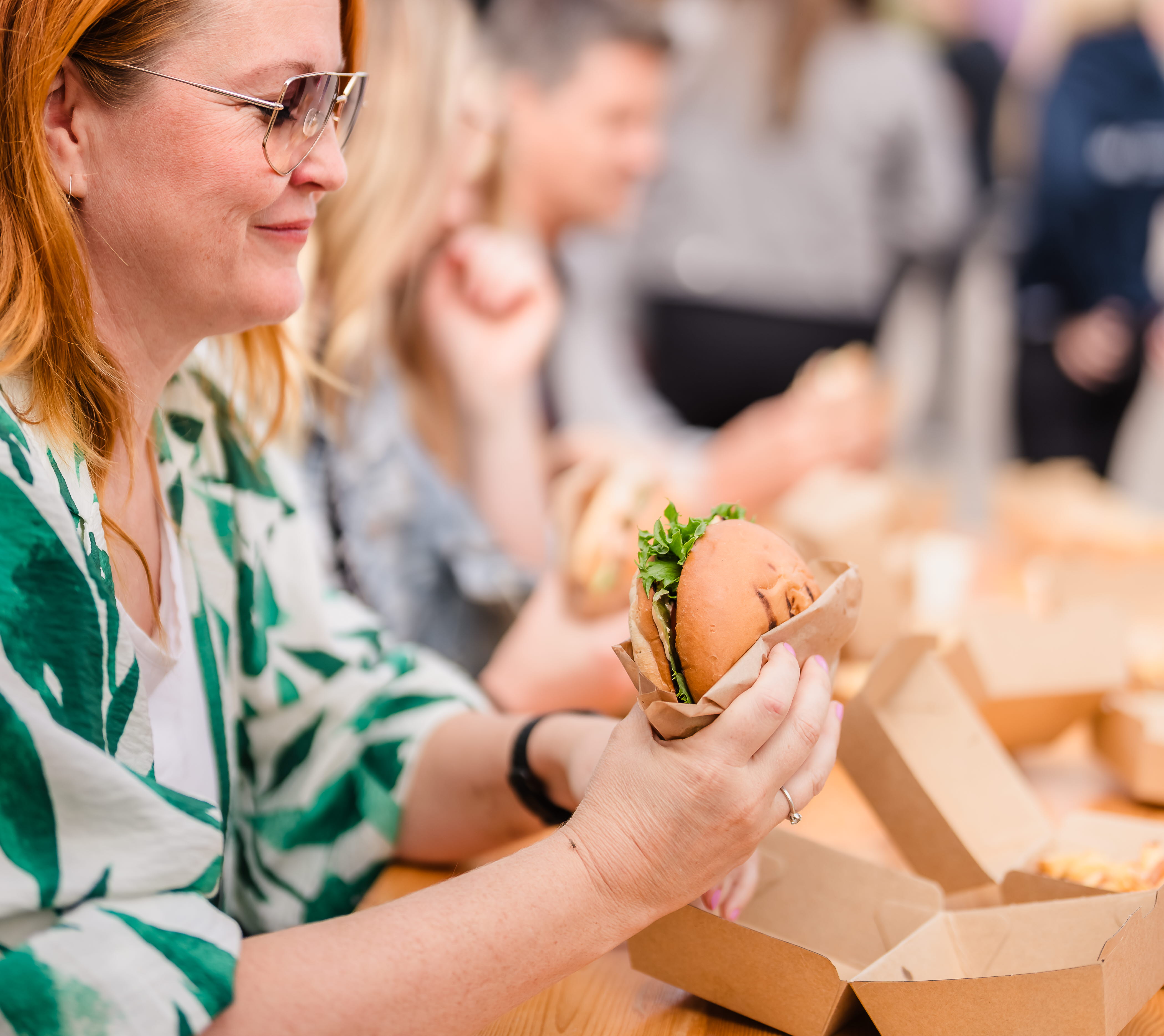 Kvinna sitter vid ett träbord och äter en hamburgare.