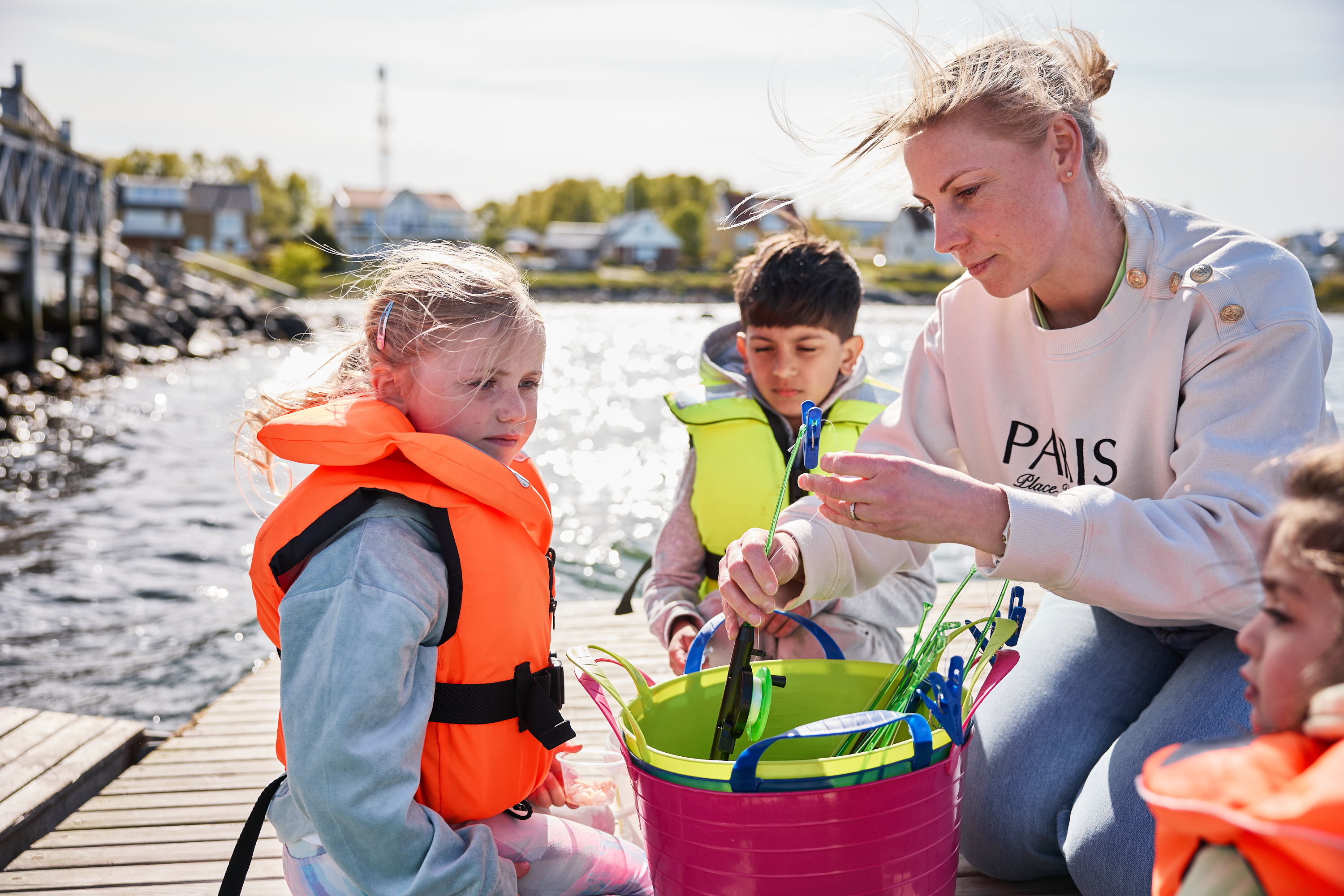 En vuxen och flera barn fiskar krabbor från en brygga med hjälp av linor och hinkar.