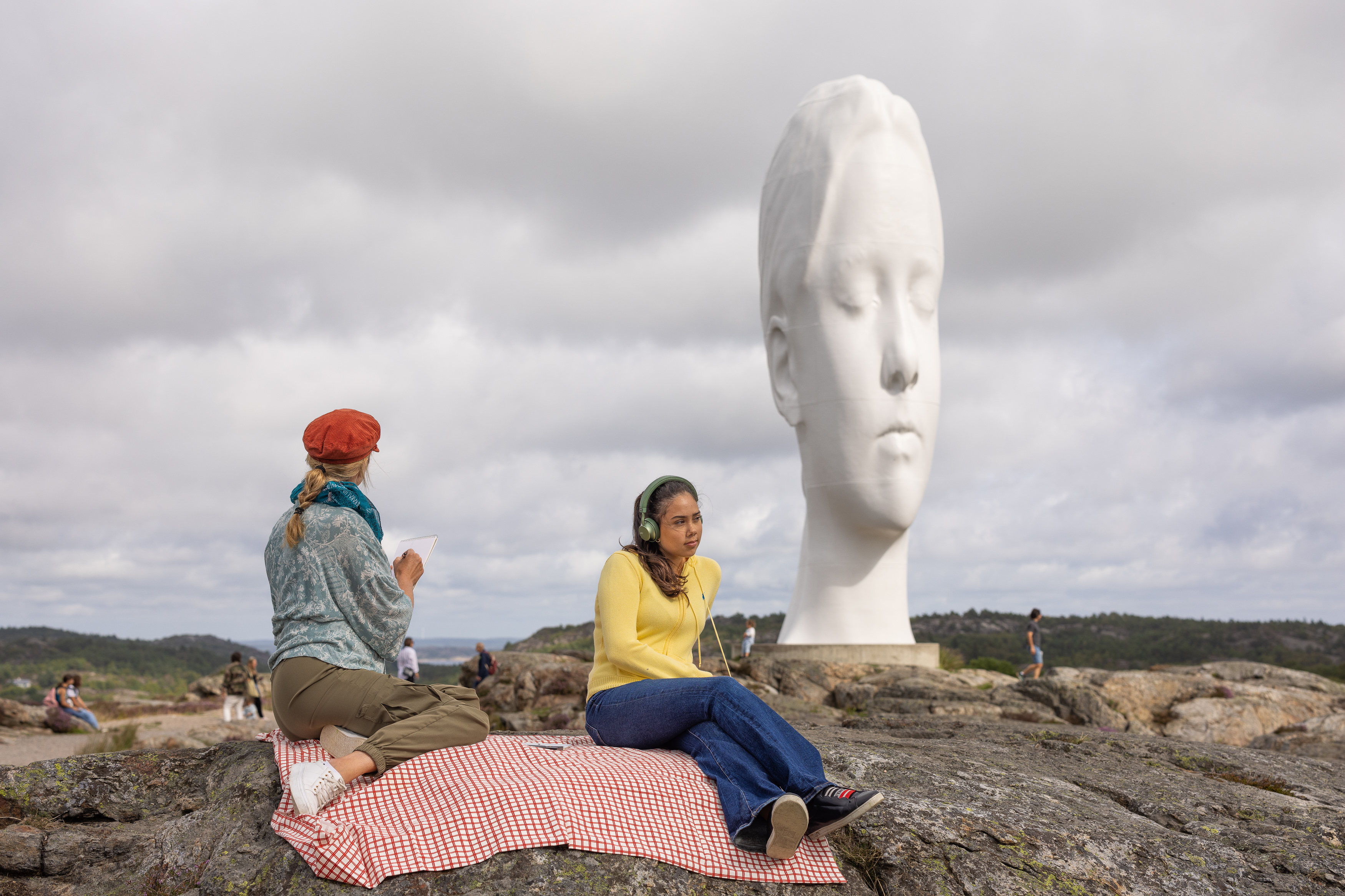 Två kvinnor sitter på en klippa i en skulpturpark.