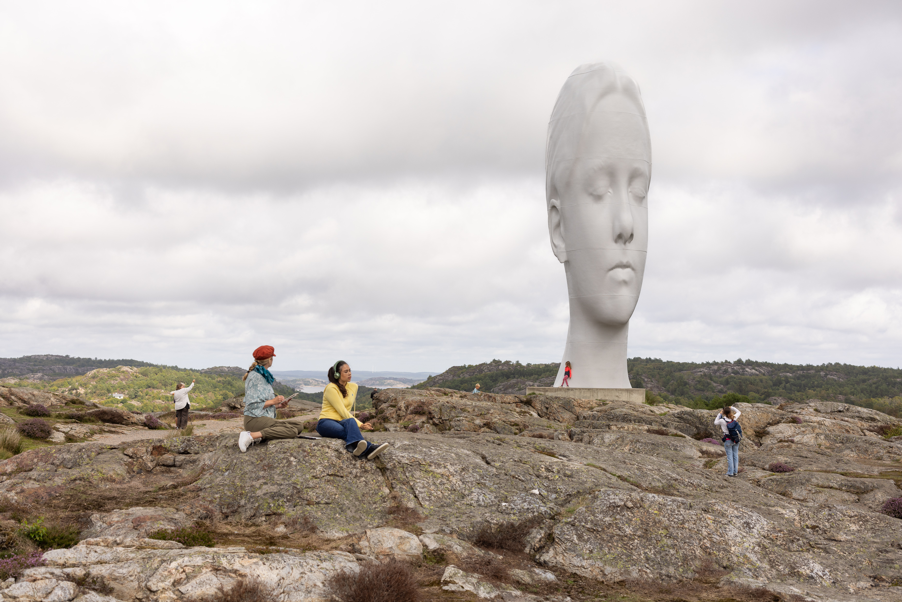 Two women sit on a rock in a sculpture park.
