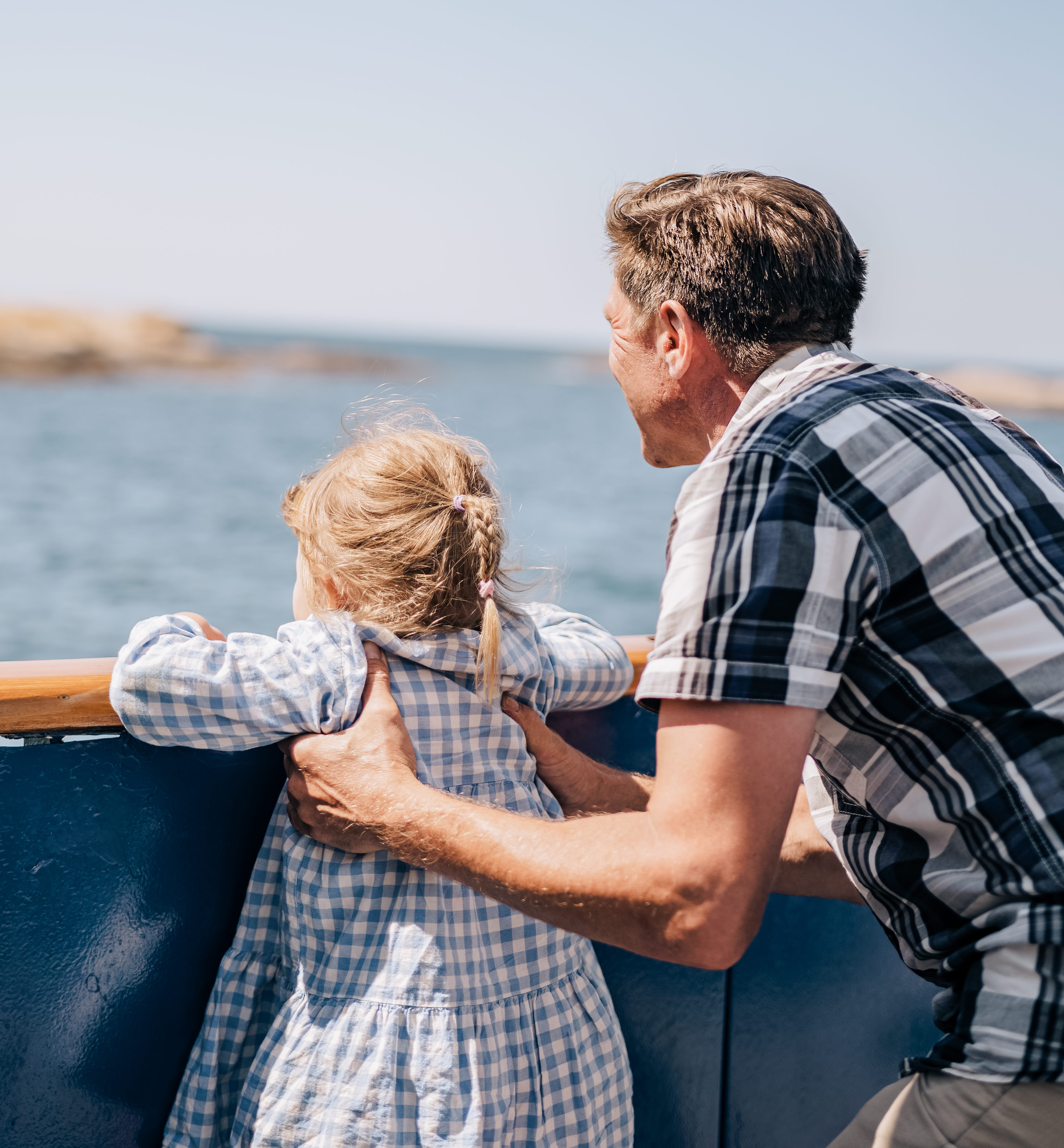 En man håller en liten flicka så att hon kan titta över en reling.