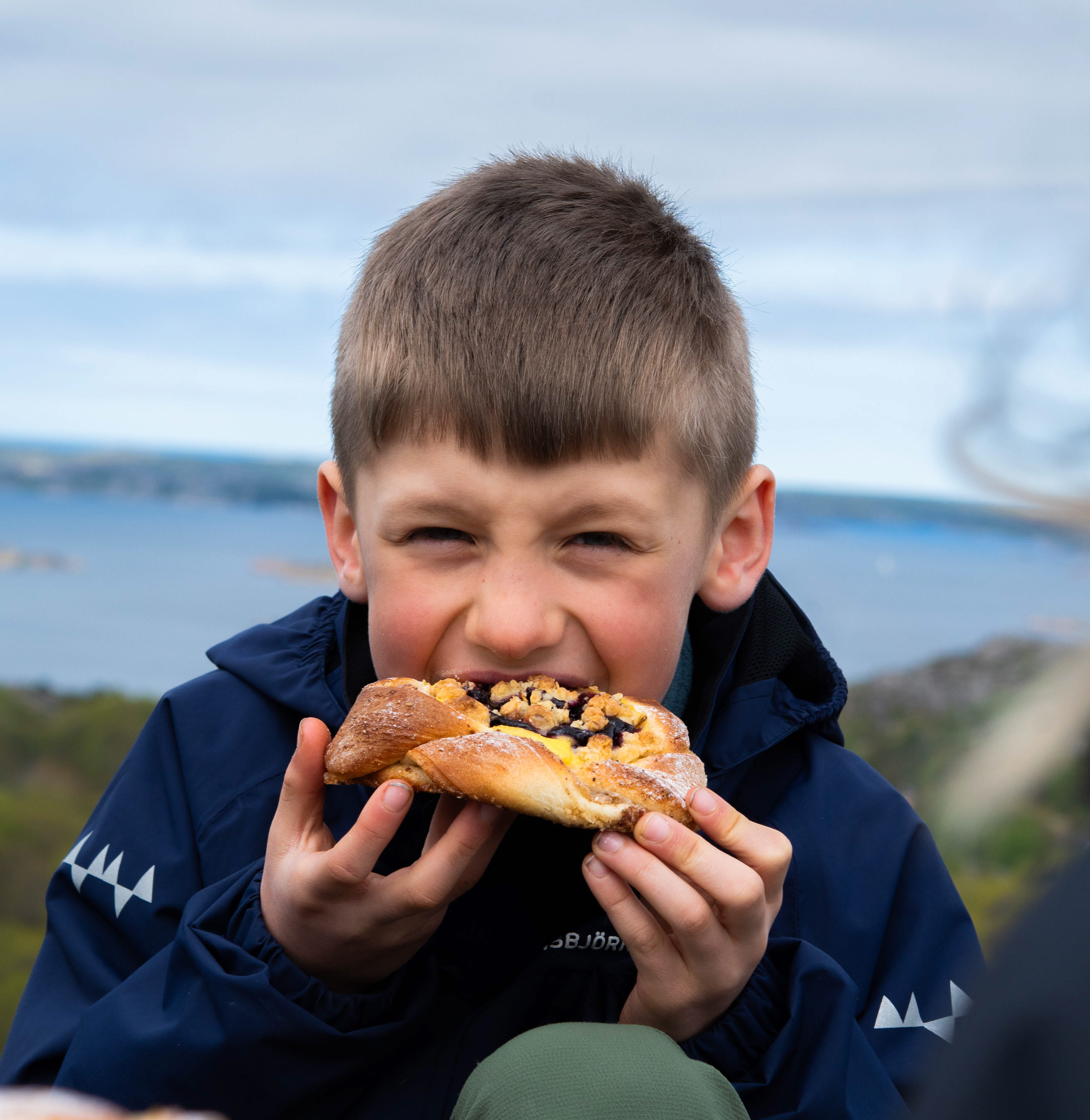 Boy eating a bun on a rock.