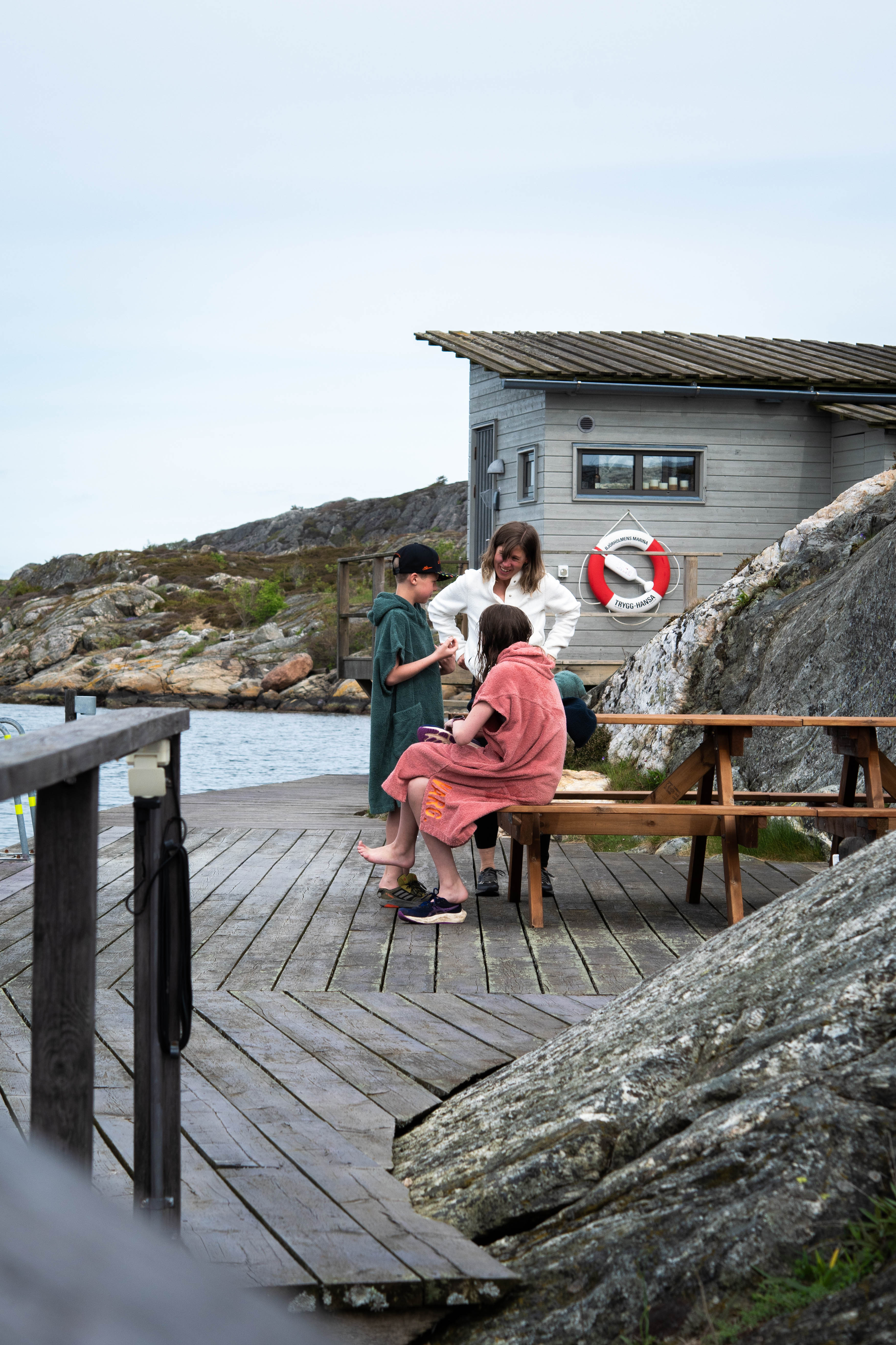 Familj som badat och står på en brygga insvepta i handdukar.