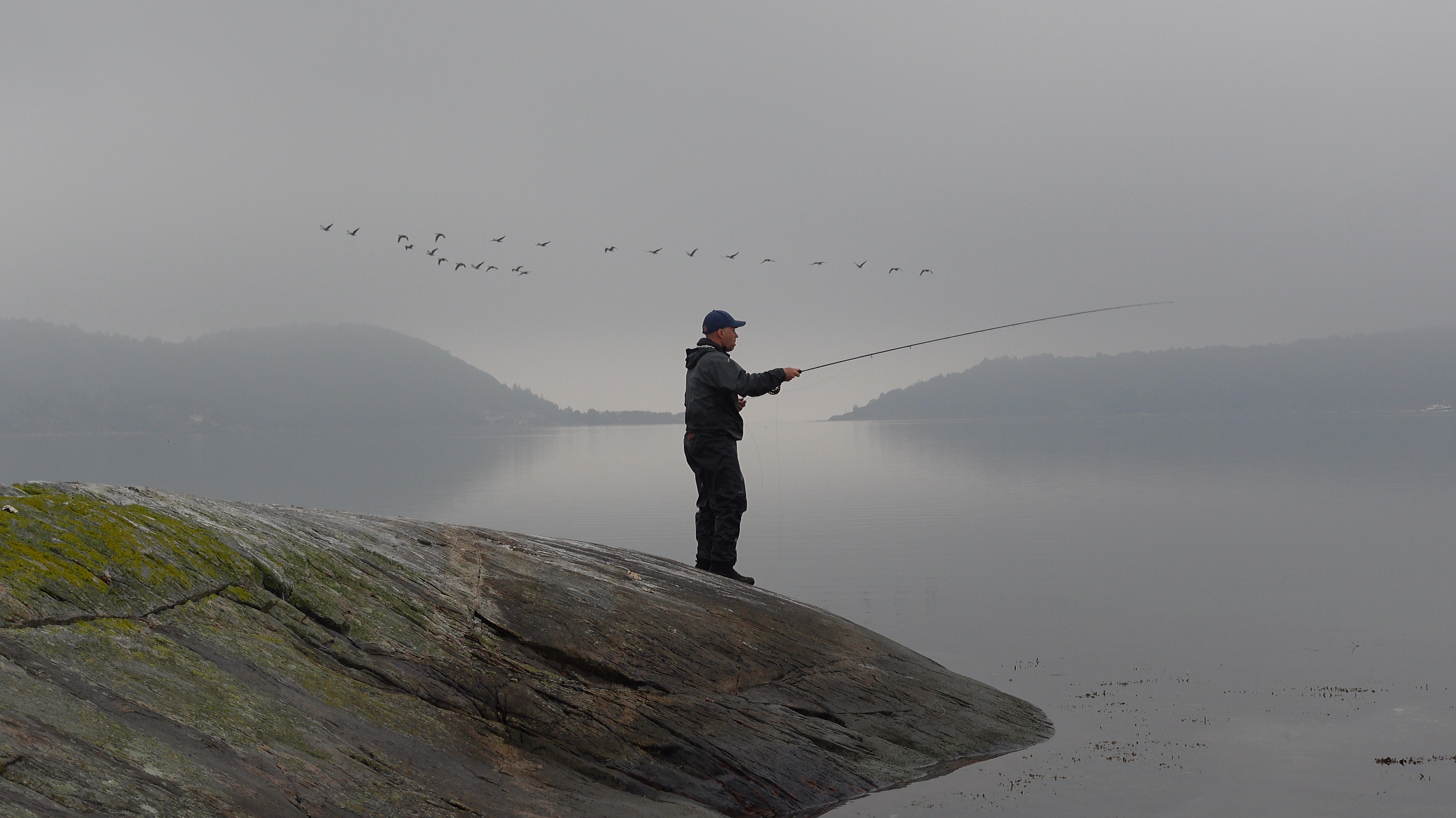 En man står på en klippa med sitt fiskespö.