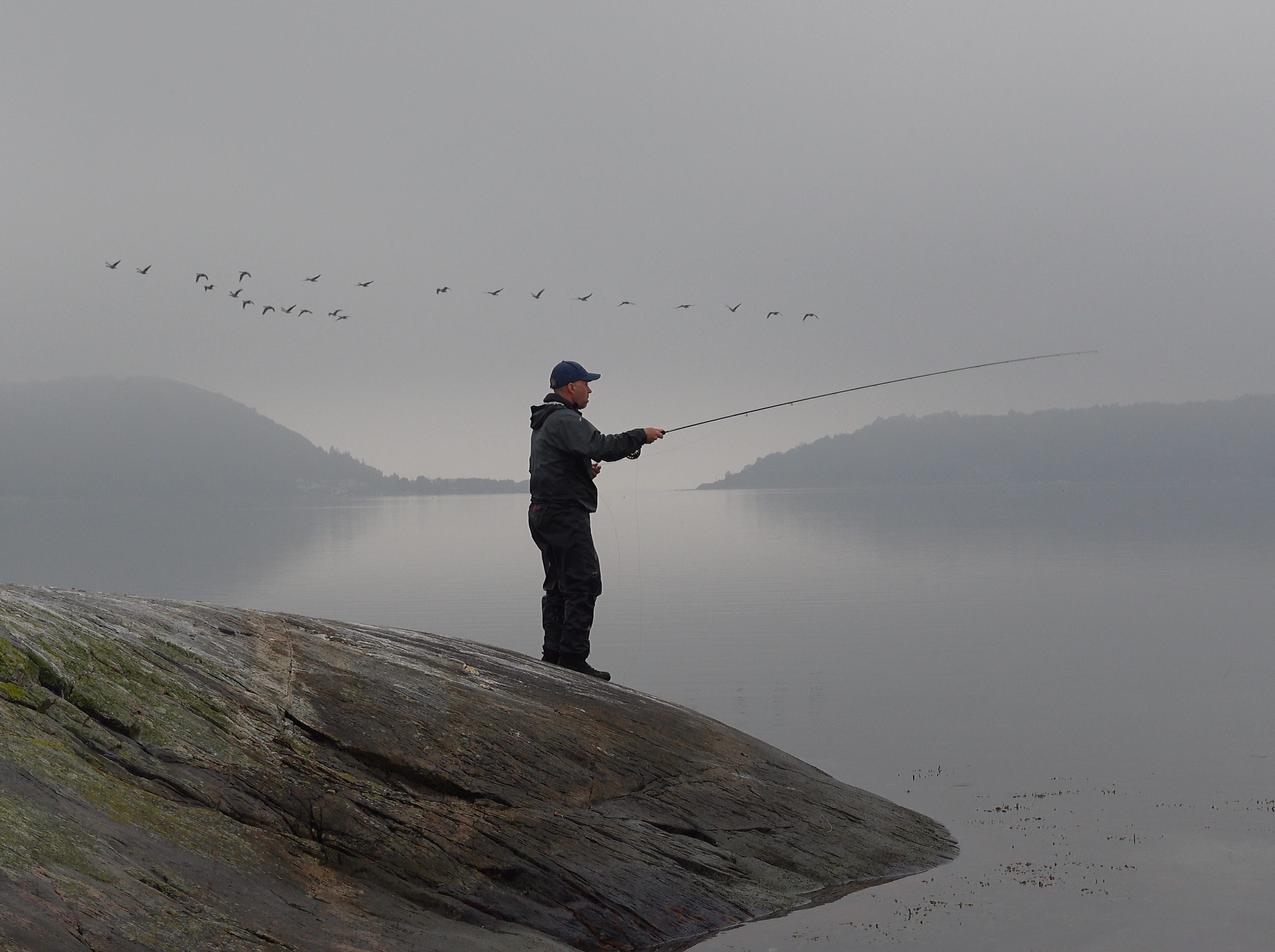 A man stands on a rock with his fishing rod.