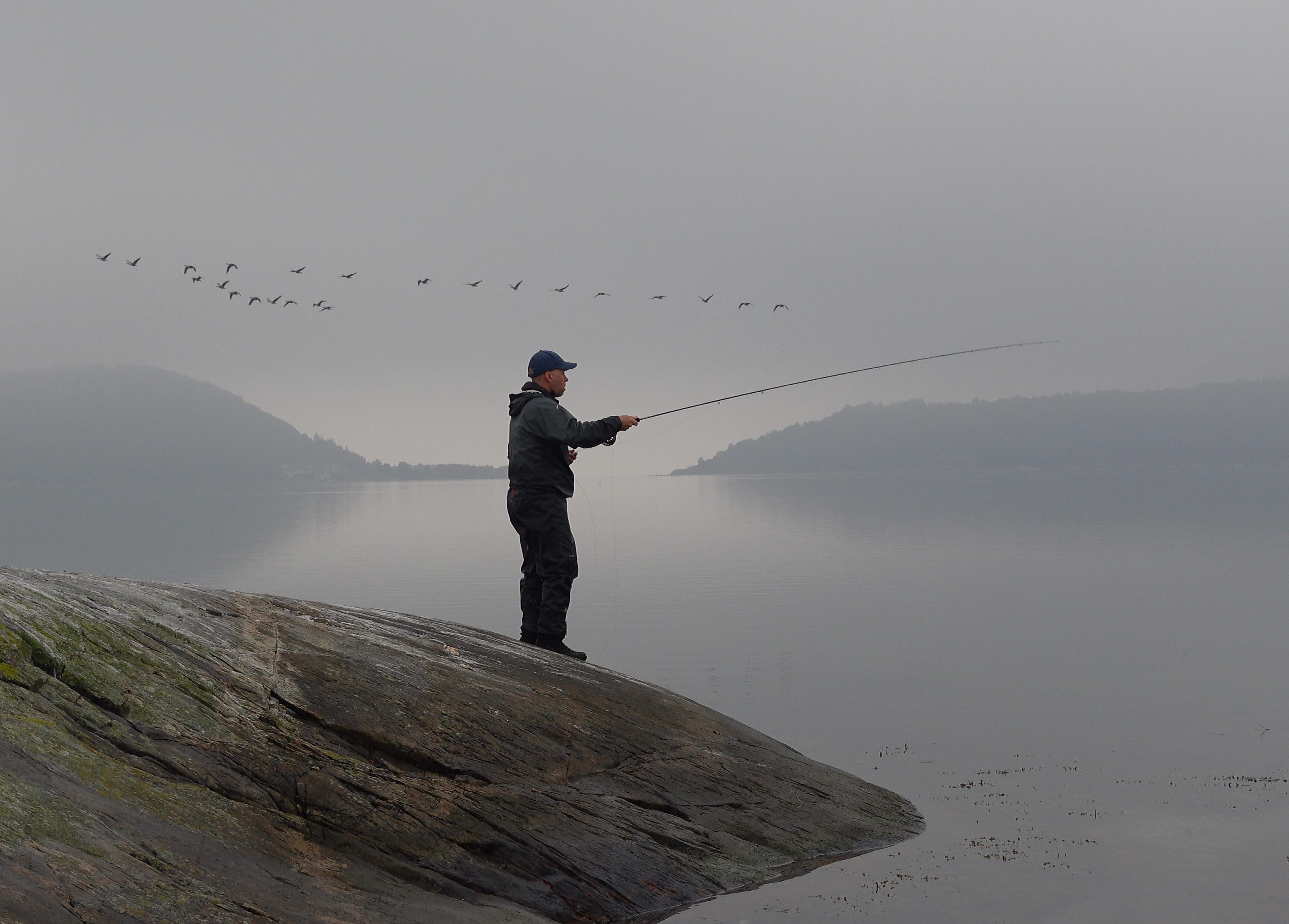 A man stands on a rock with his fishing rod.