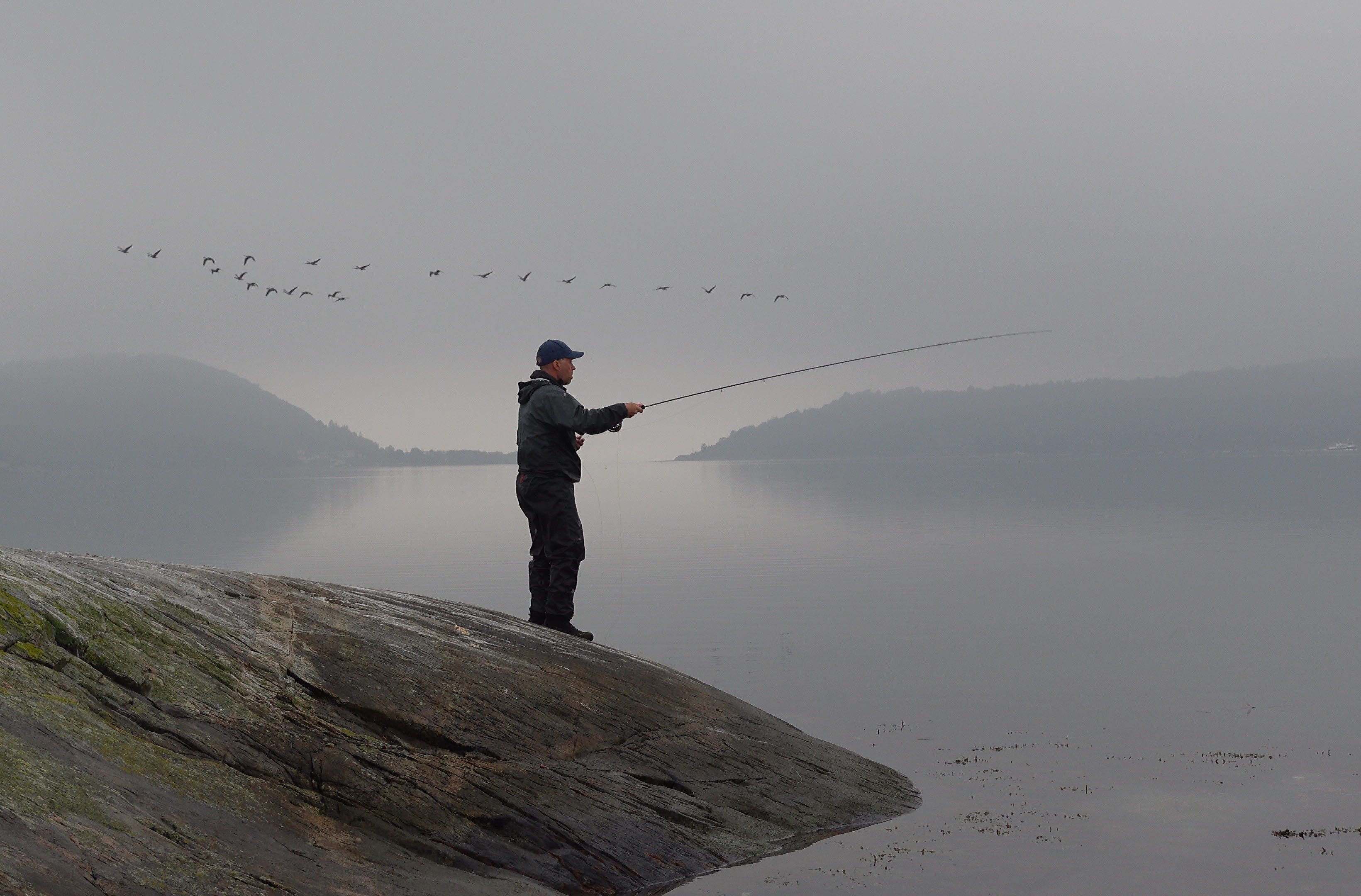 A man stands on a rock with his fishing rod.