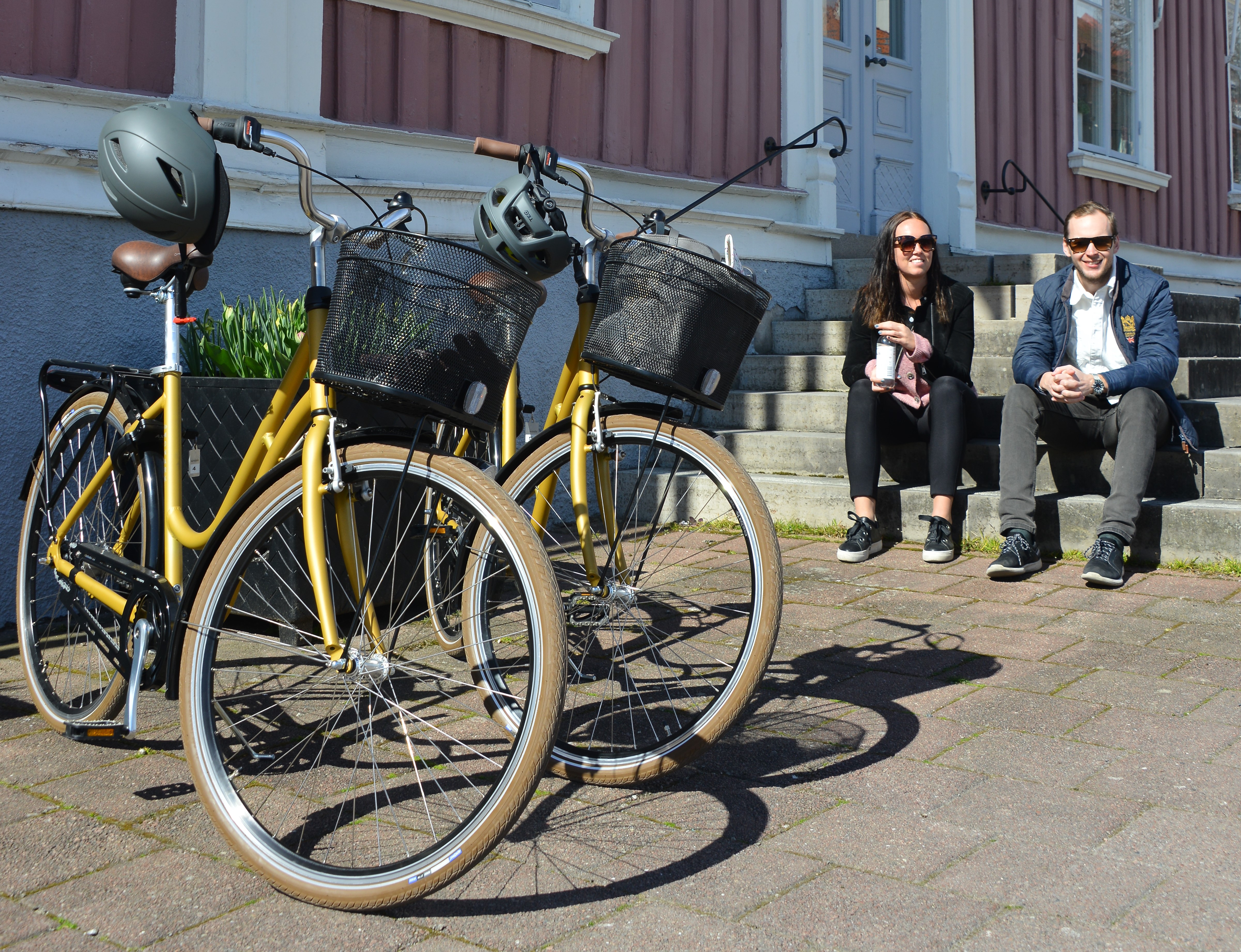 två cyklar vid en trappa där en tjej och en kille sitter ned. 