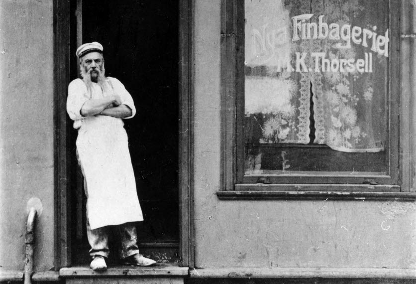 A baker stands in the front door of a bakery.