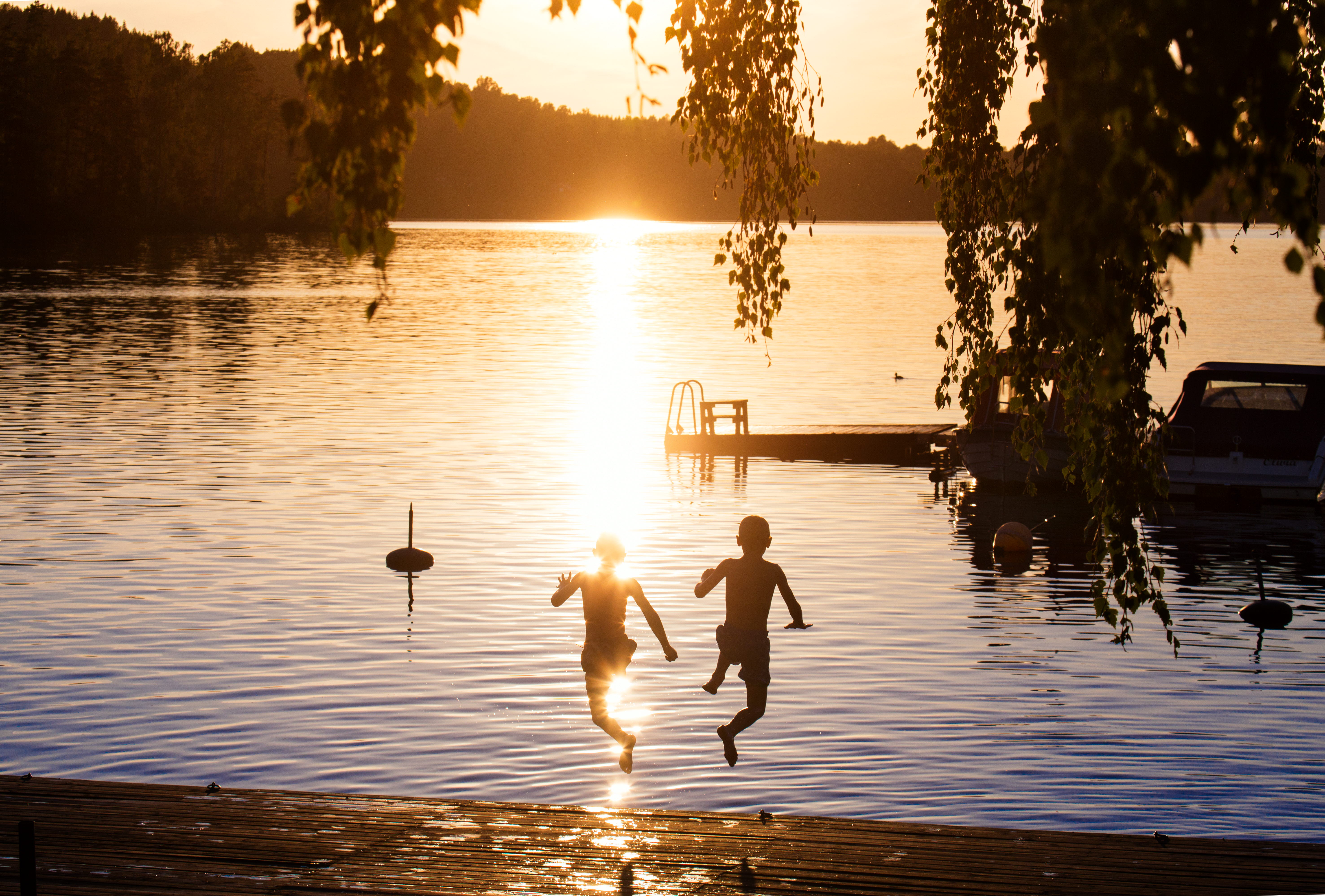 barn som hoppar i vattnet i solnedgång. 