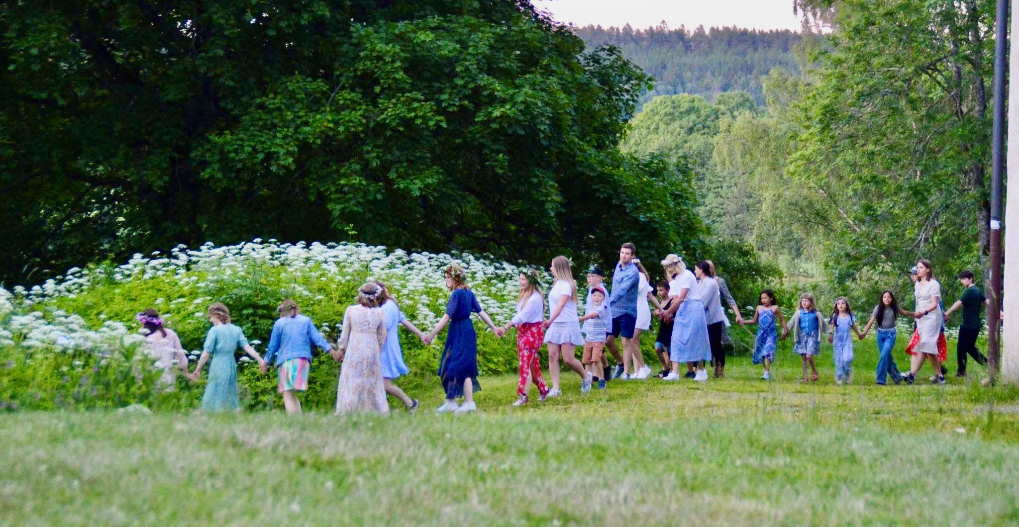 Människor dansar i gräset på midsommarafton.