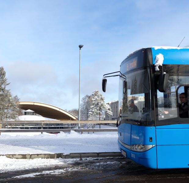 Framdelen av en blå bussar, i bakgrunden ser du snö och skog, en människa går ut ur bilden till vänster.