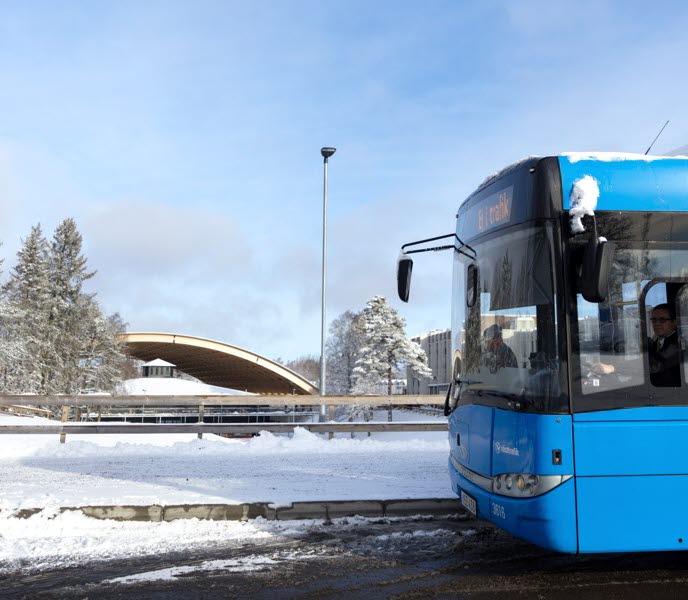 Framdelen av en blå bussar, i bakgrunden ser du snö och skog, en människa går ut ur bilden till vänster.