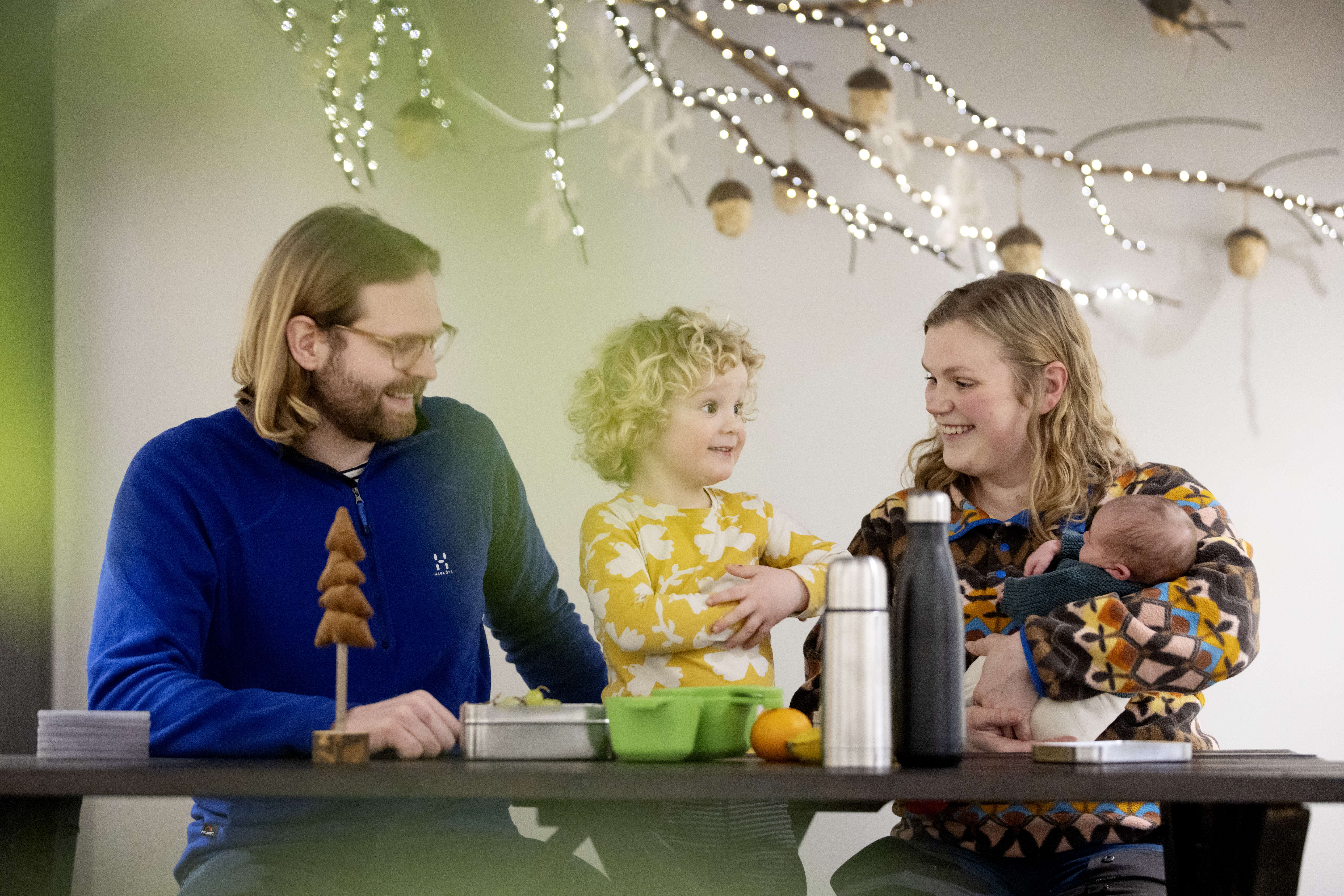 Familj pappa, son och mamma med bebis i famnen sitter och fikar medhavd matsäck inomhus (i Billingecenter på Billingen Skövde.)