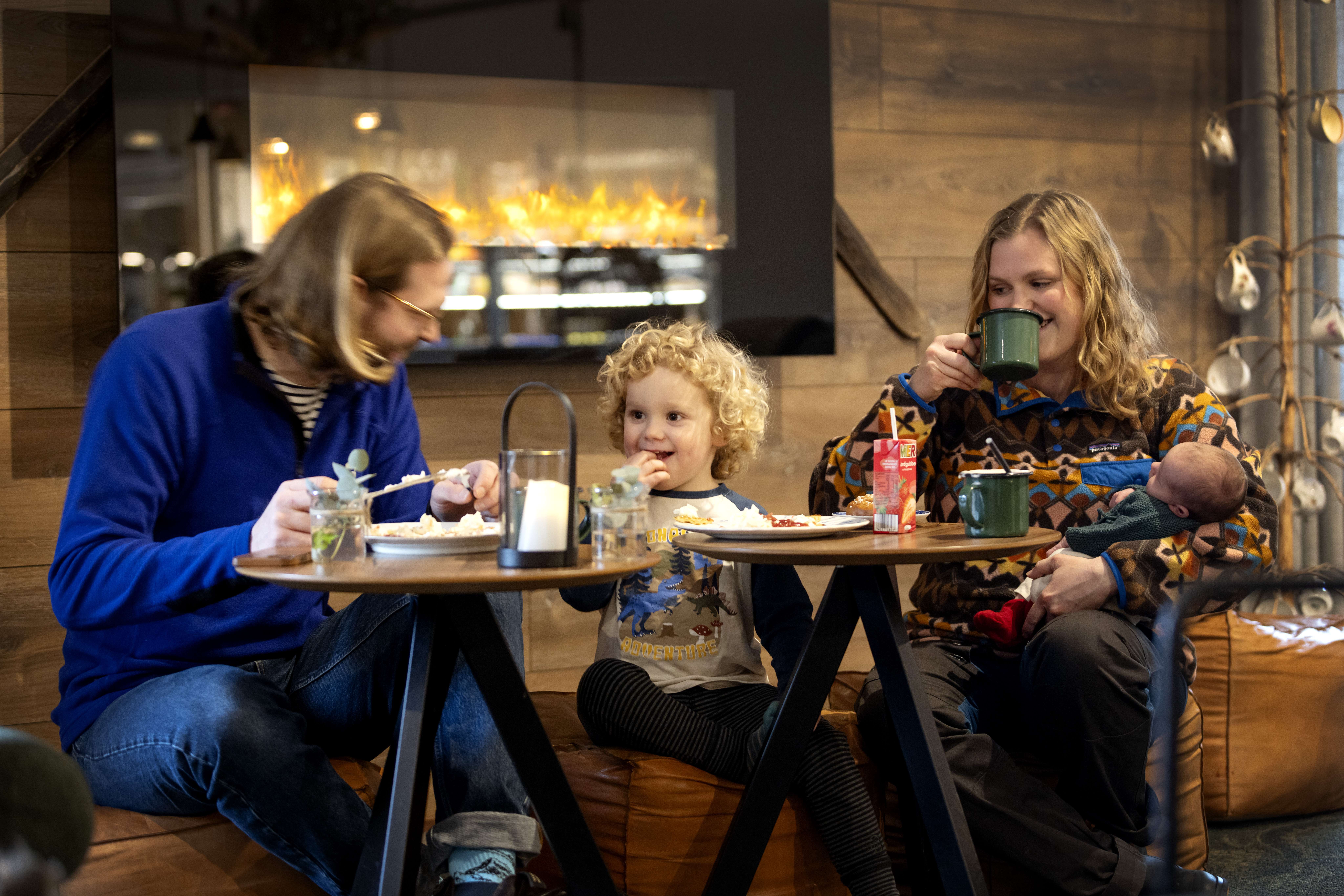 Father, son and mother with a small baby in their arms are sitting in front of the fire, eating and laughing.