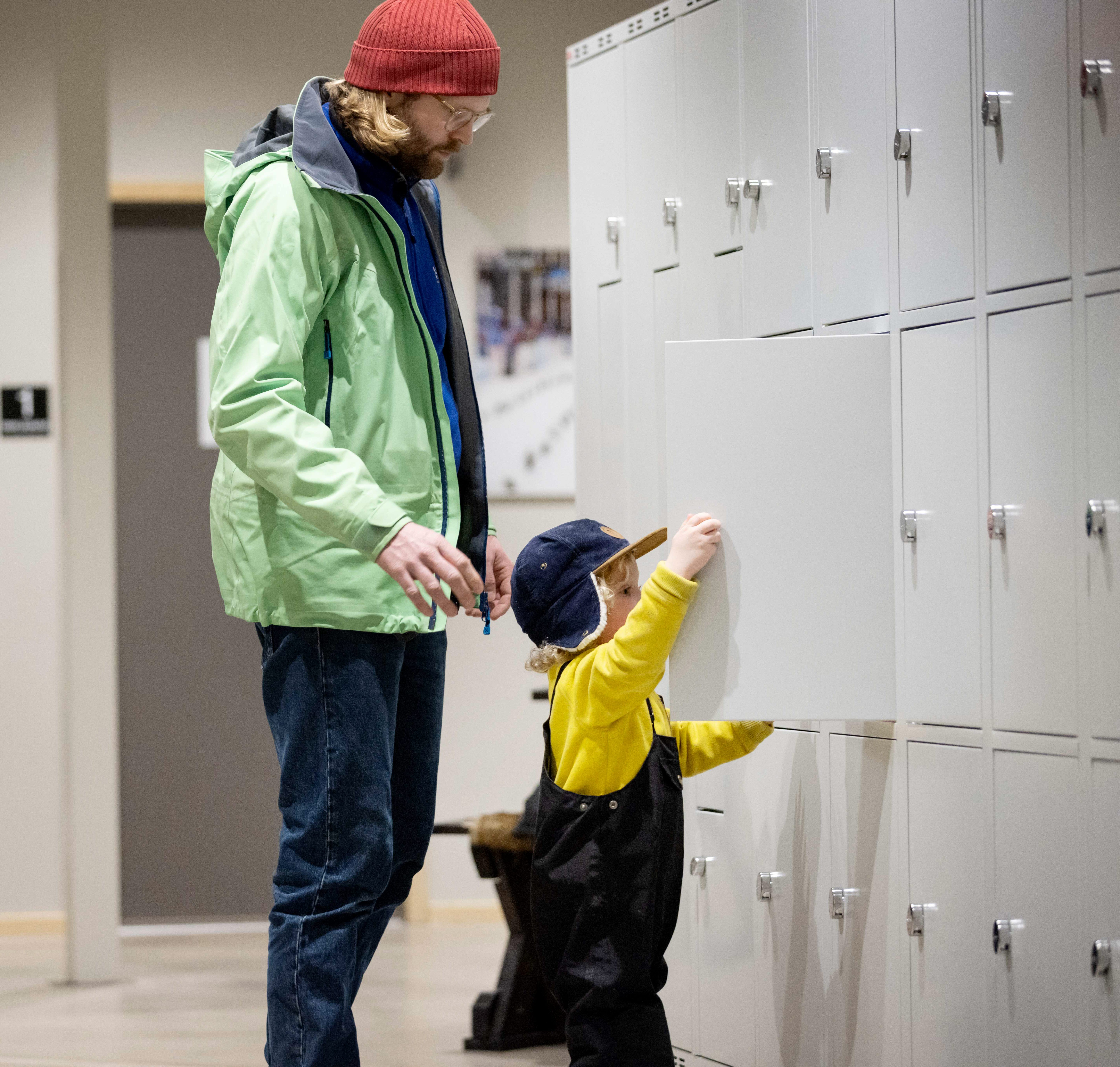 One wall is covered with storage cabinets. A small guy stands and closes one of the cupboards. Behind him is his father.