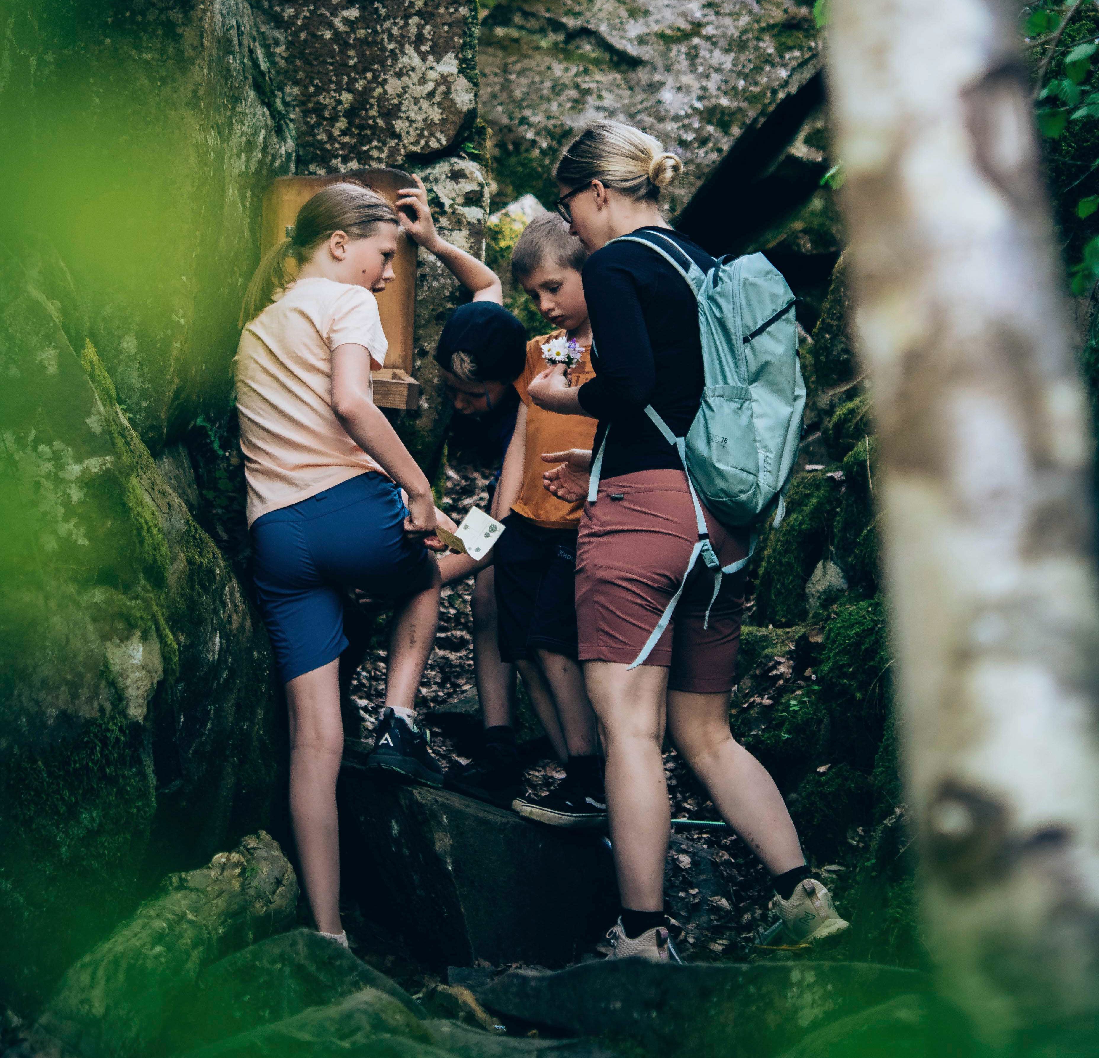 Mamma och barn vandrar i skogen står vid klippblock