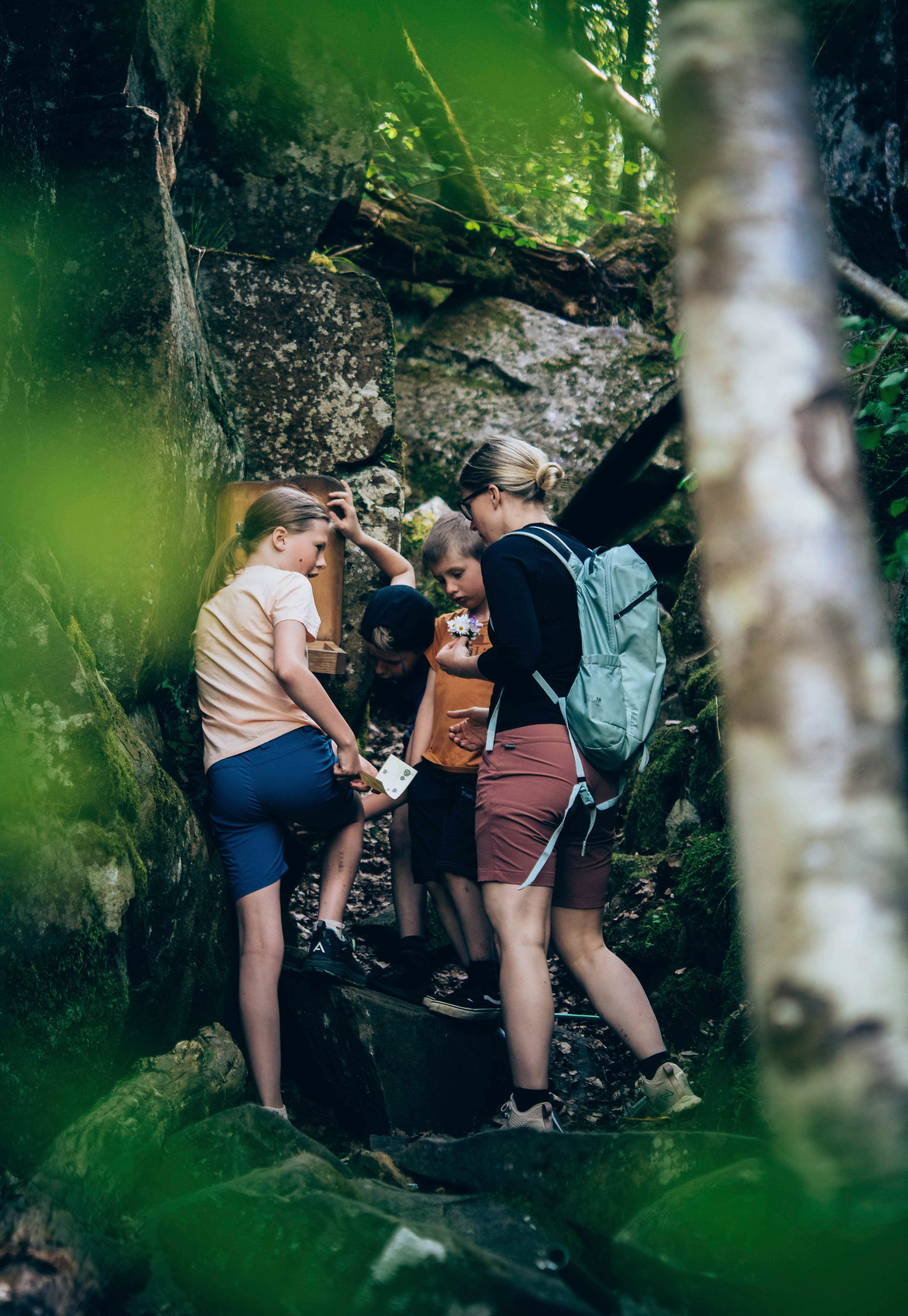 Mamma och barn vandrar i skogen står vid klippblock