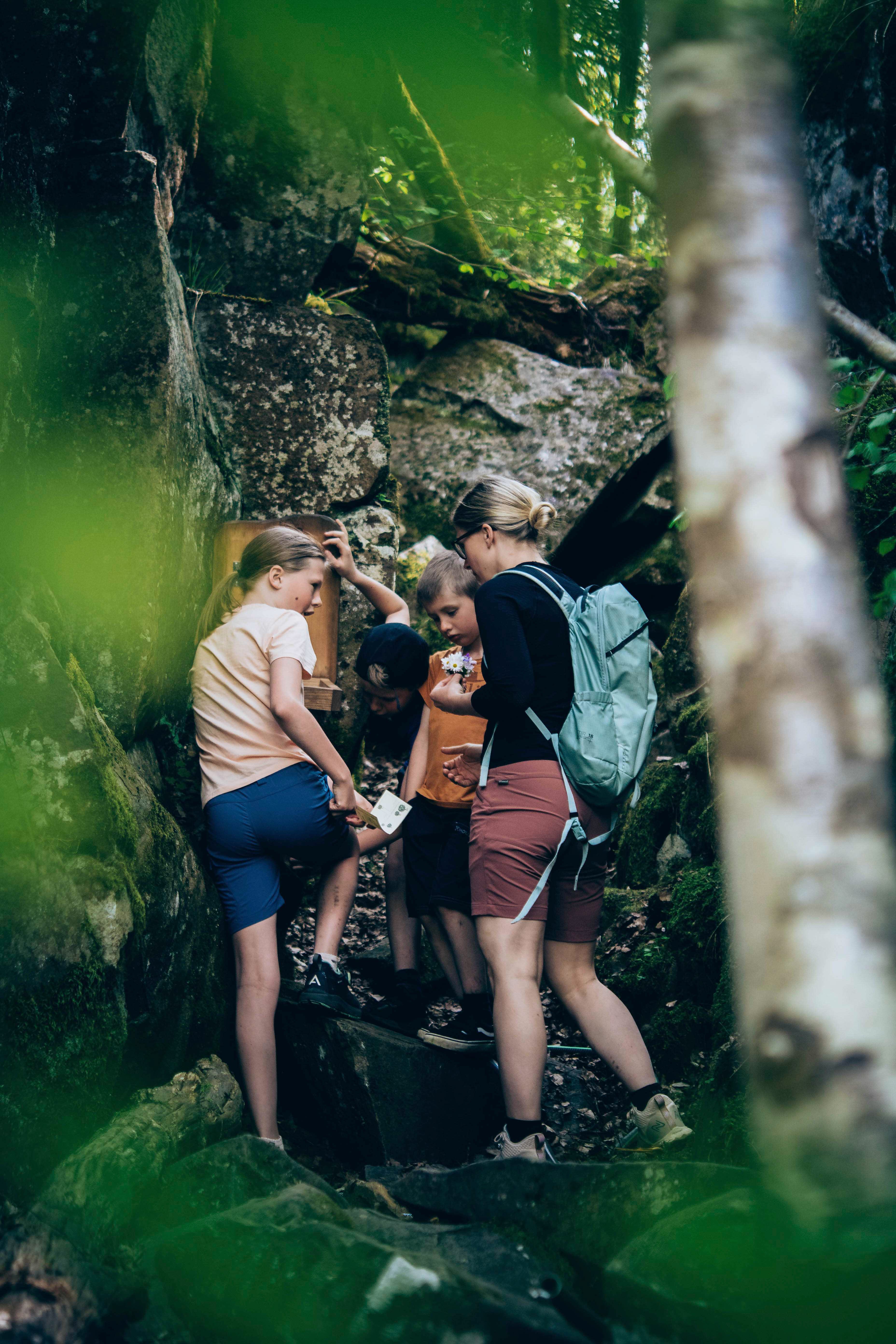 Mamma och barn vandrar i skogen står vid klippblock