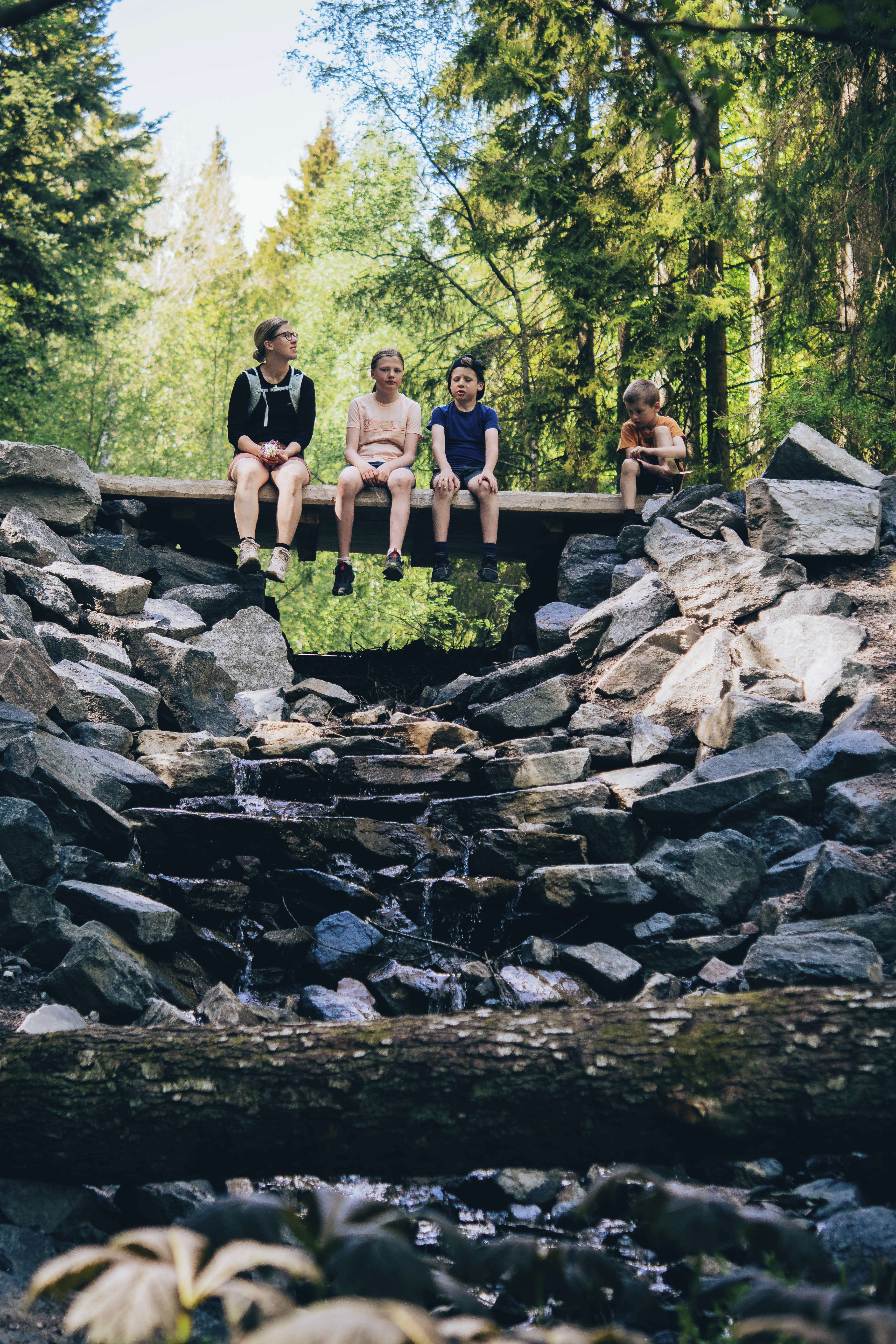 Fyra barn sitter på träbro över stenig bäck