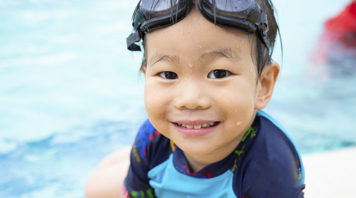 Liten pojke sitter vid pool med simglasögon i pannan