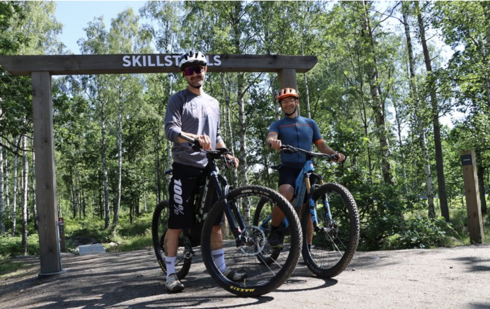Two men stand with their mtb in front of a portal that says Skillstrails