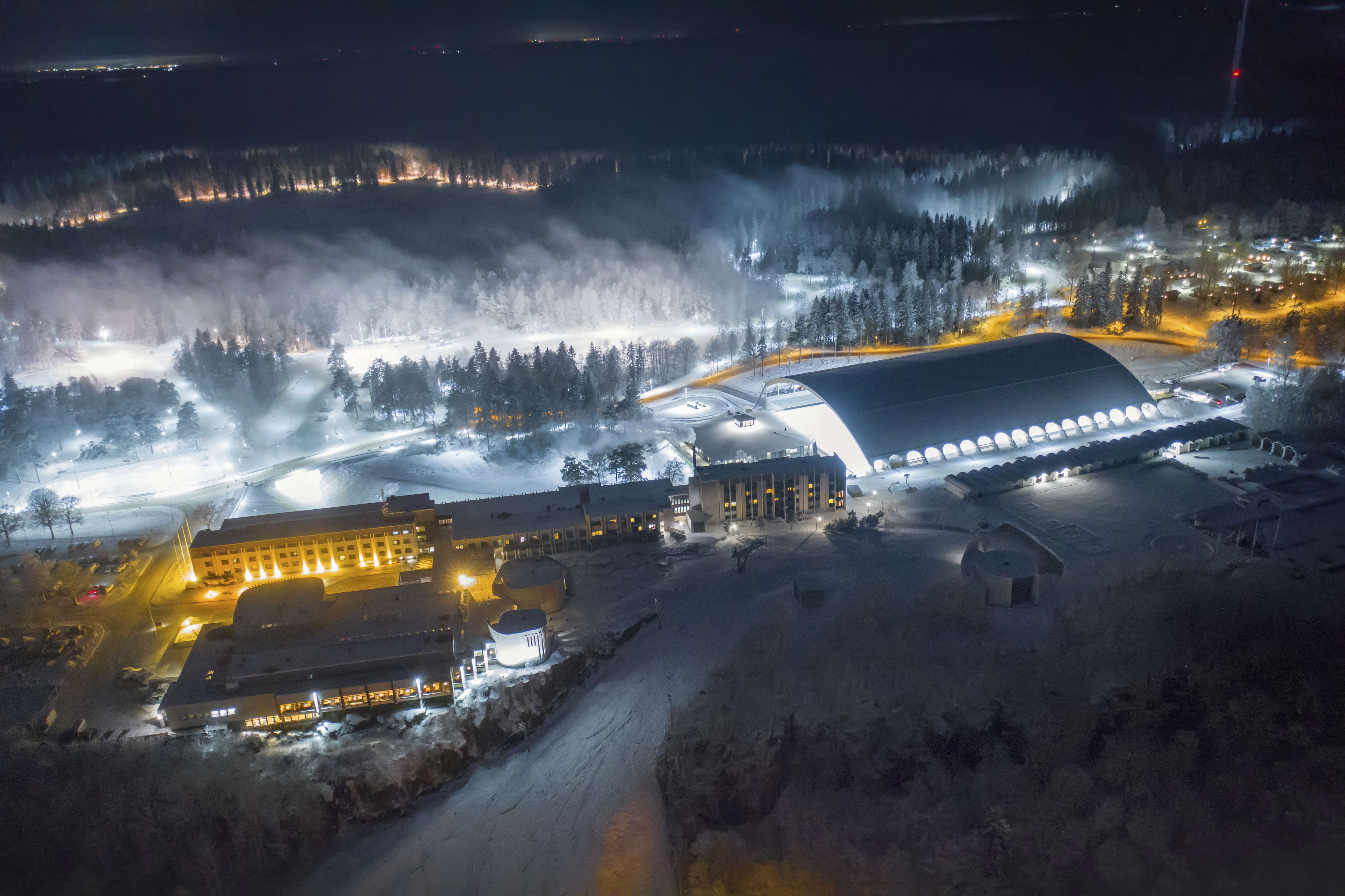 Drönarbild över Billingen Skövde en vinterkväll. Du kan se de upplysta skidspåren, isbanan, hotellet, camping och i förgrunden slalombacken.