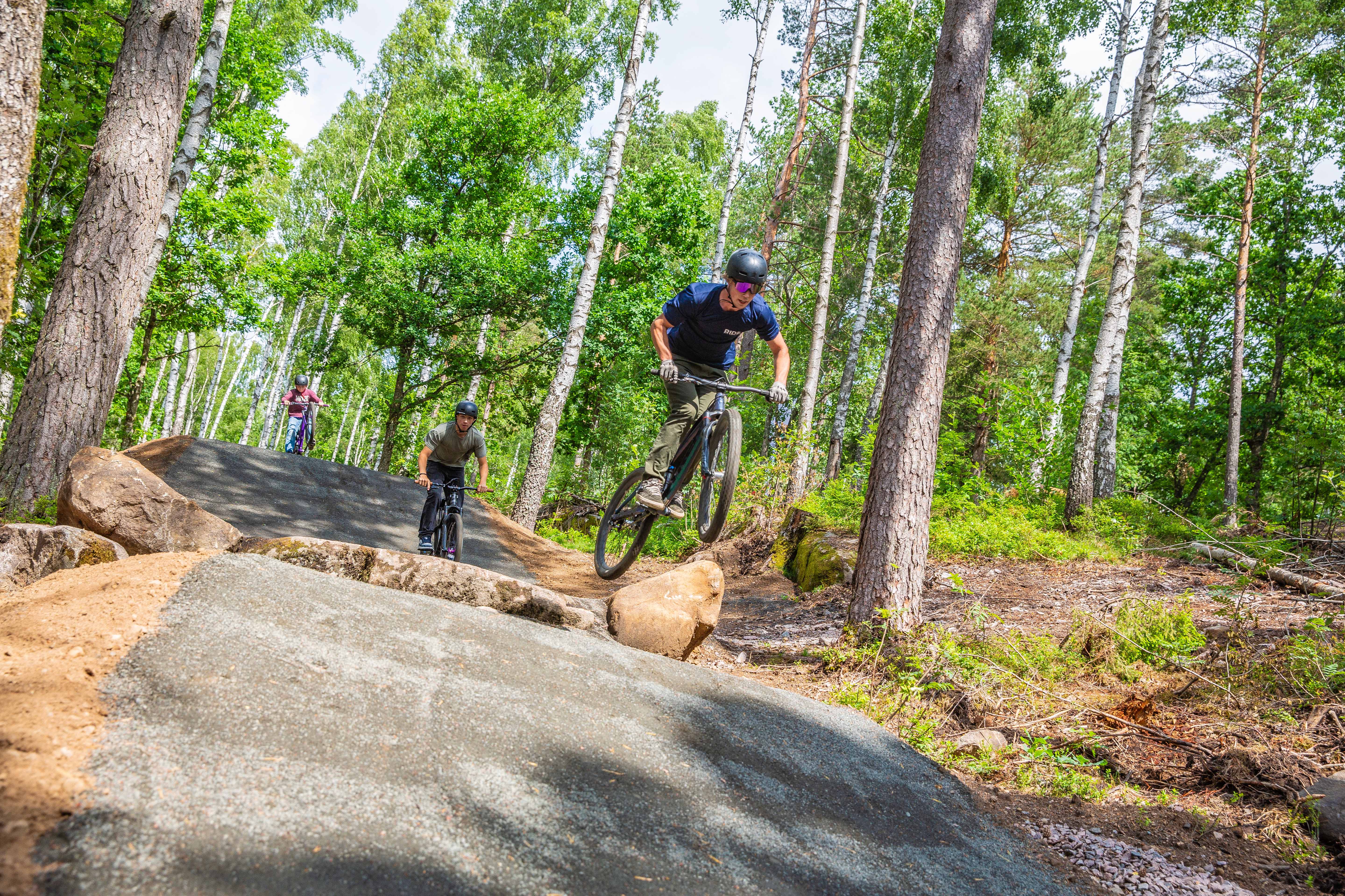 En person i mörka kläder och hjälm cyklar och hoppar över byggda gupp på en bana. 