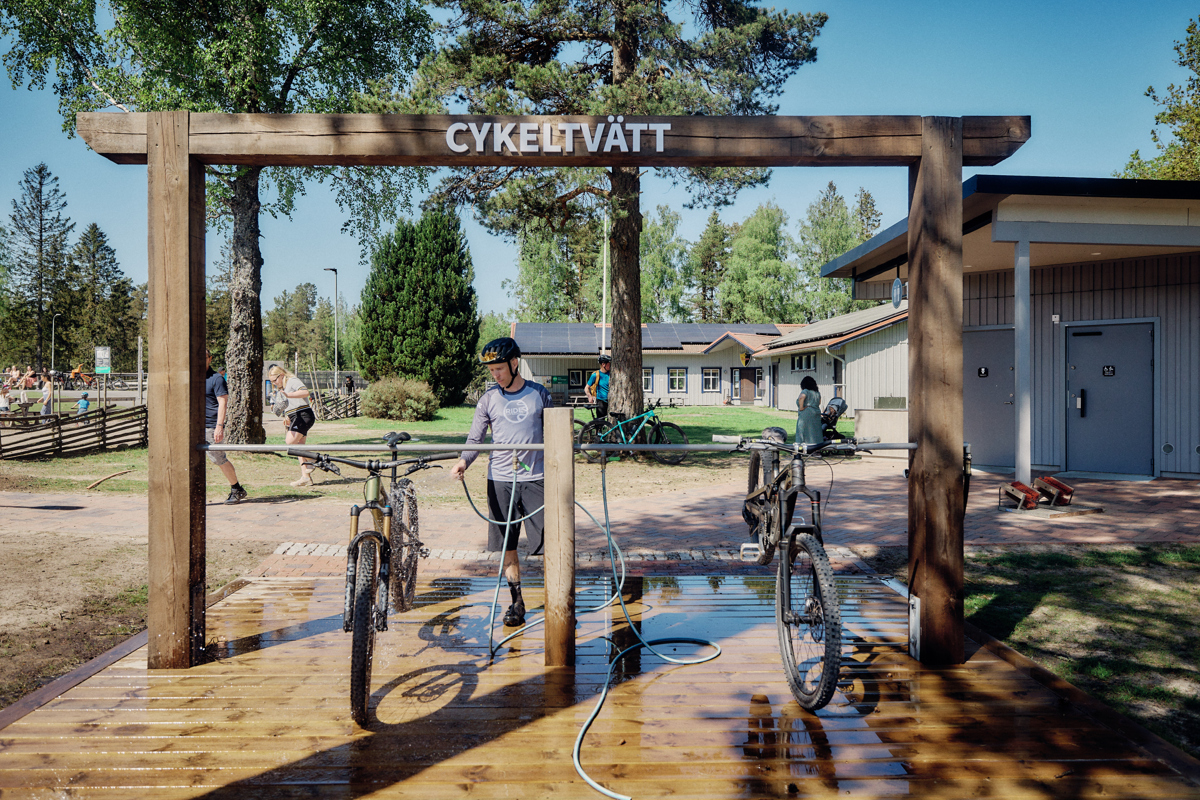 A man standing next to two bikes on a wooden platform holding a water hose