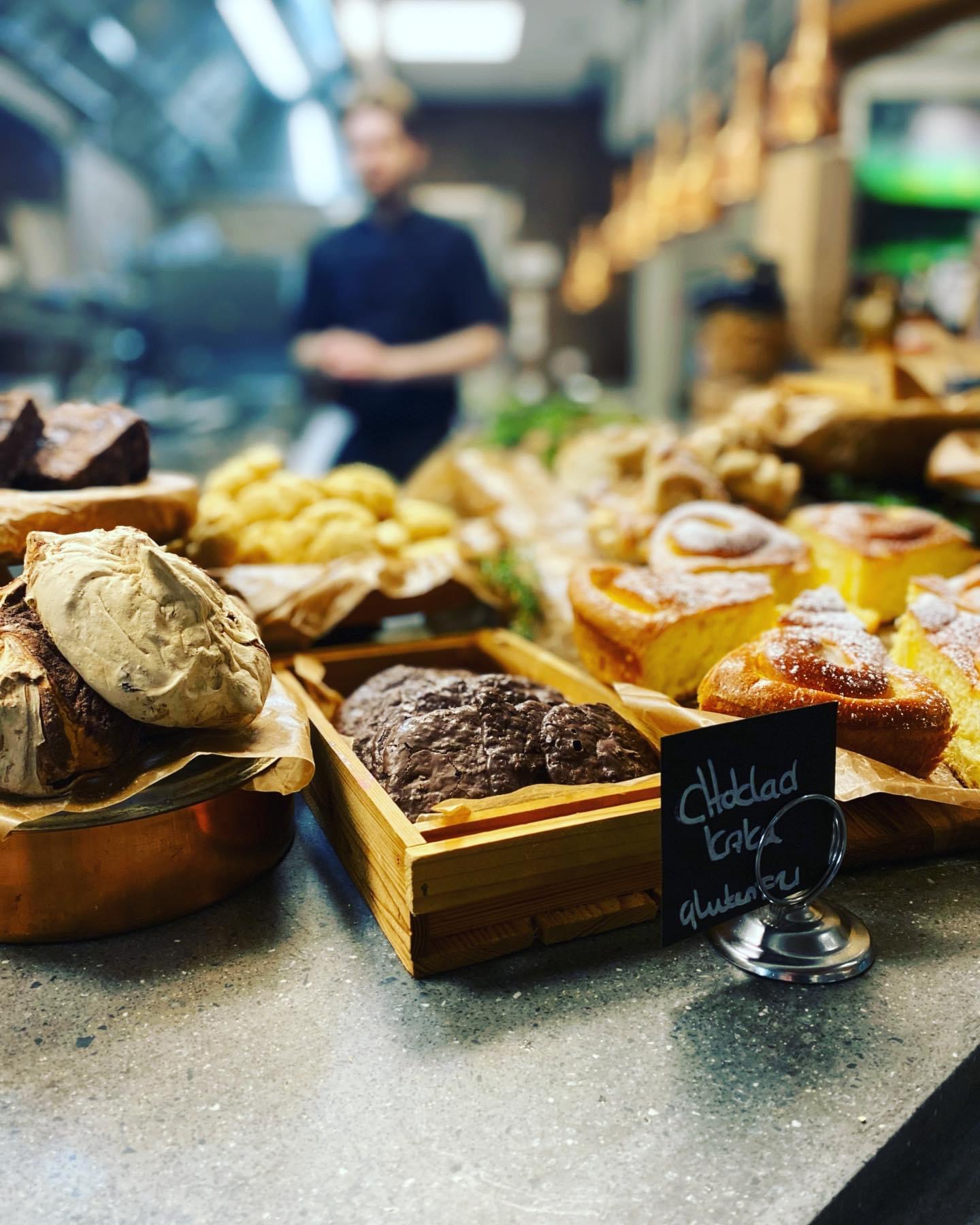 Bullar och kakor är härligt skyltade i trälådor och tråg på en disk, i bakgrunden symtas en restaurangkök. 