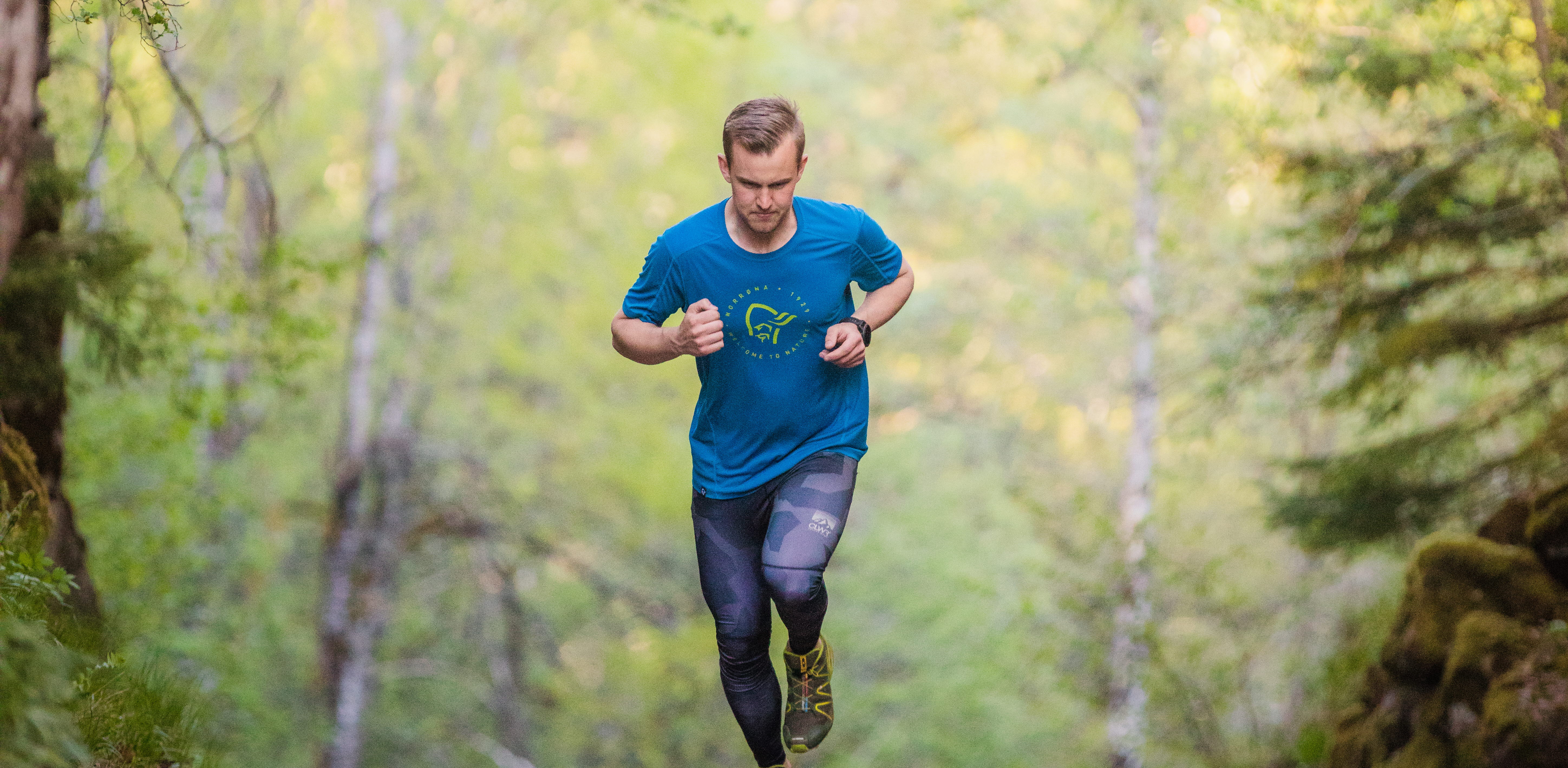 Man som springer i uppförsbacke med grönskande träd runt omkring sig. 