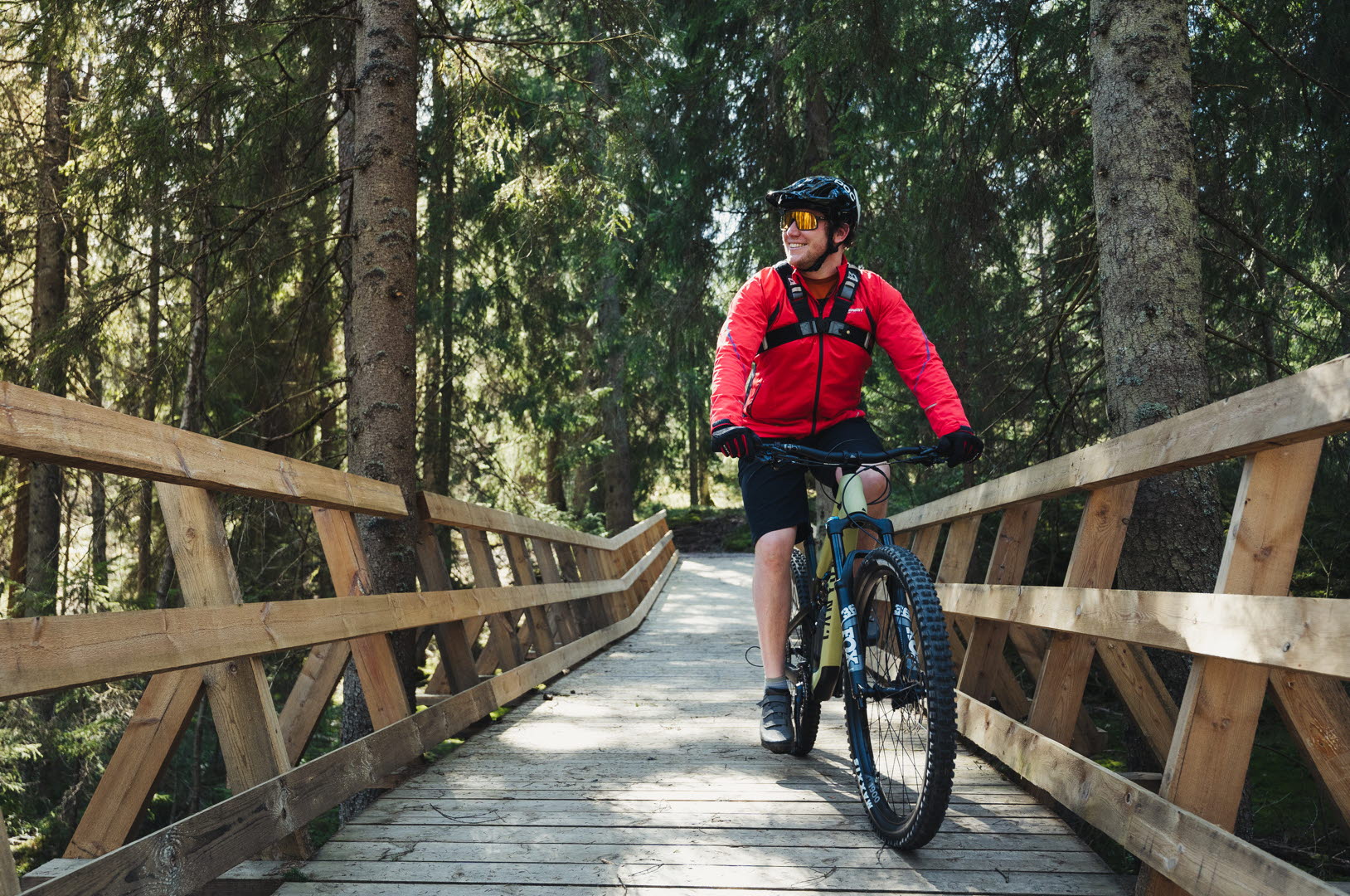 Man cyklar mountainbike på en byggd träbro i skogen. 