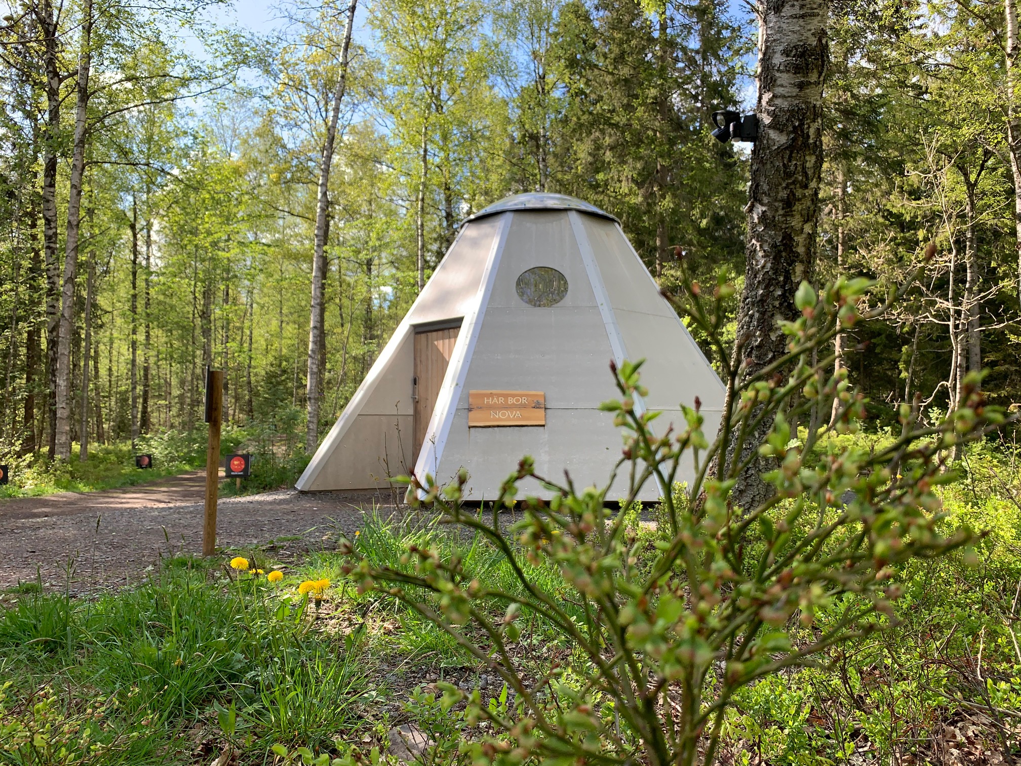 Ett beige tältformat hus mitt i grönskande omgivningar. 