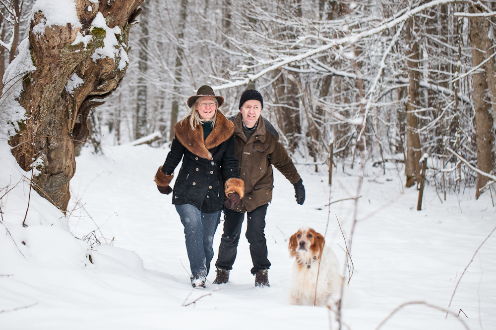 En kvinna och en man är ute i skogen och vandrar i snön med sin hund.