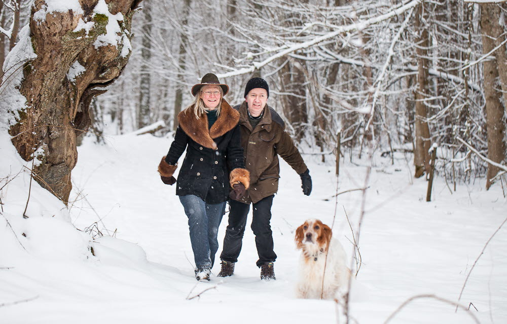 En kvinna och en man är ute i skogen och vandrar i snön med sin hund.