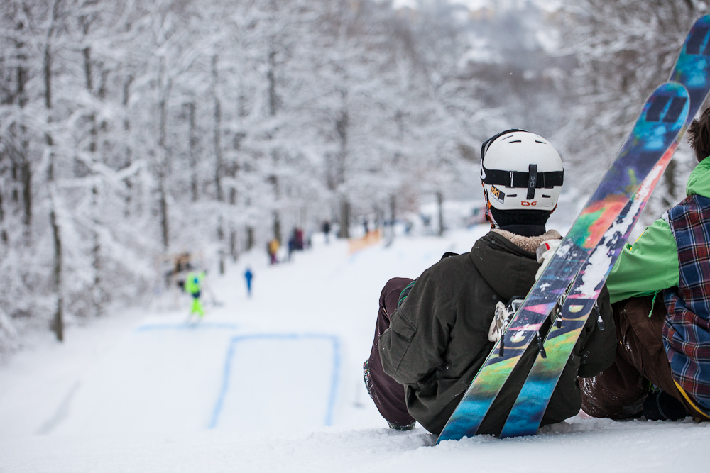 Person sitter och lutar sig mot sina skidor och blickar ut över backen. 