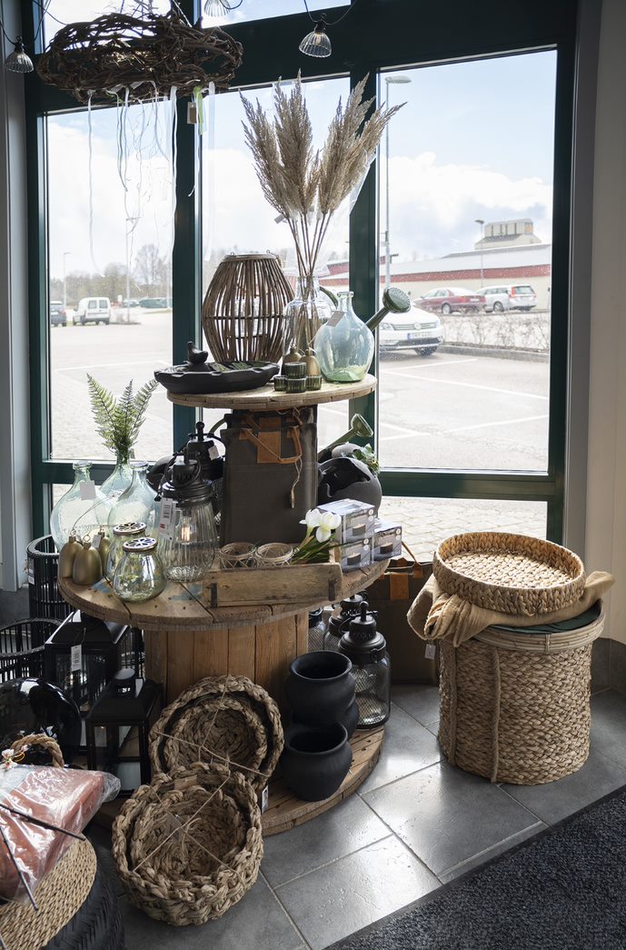 Inredningsprylar i form av krukor, ljusstakar och tvättkorg i naturnära färger som står på två kabeltunnor i trä. 