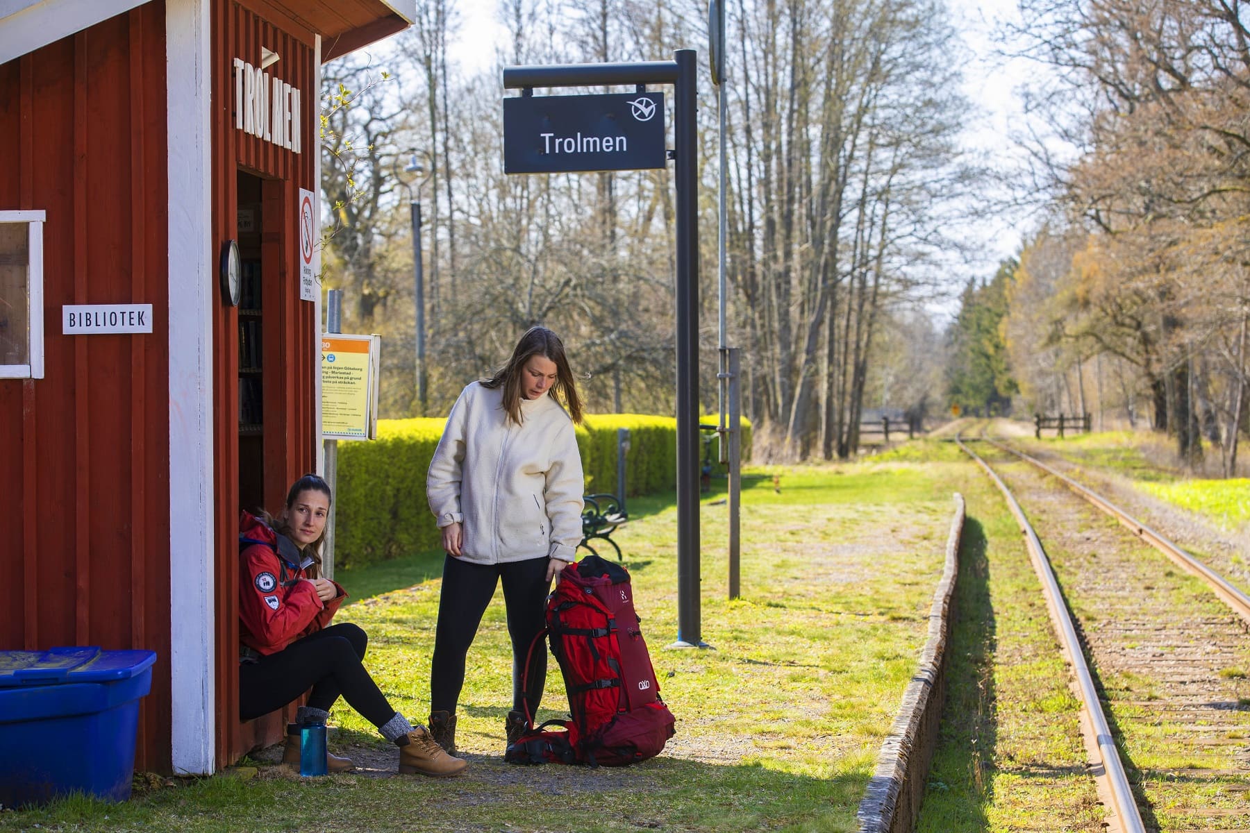 Two girls waiting on the train by a small red house.