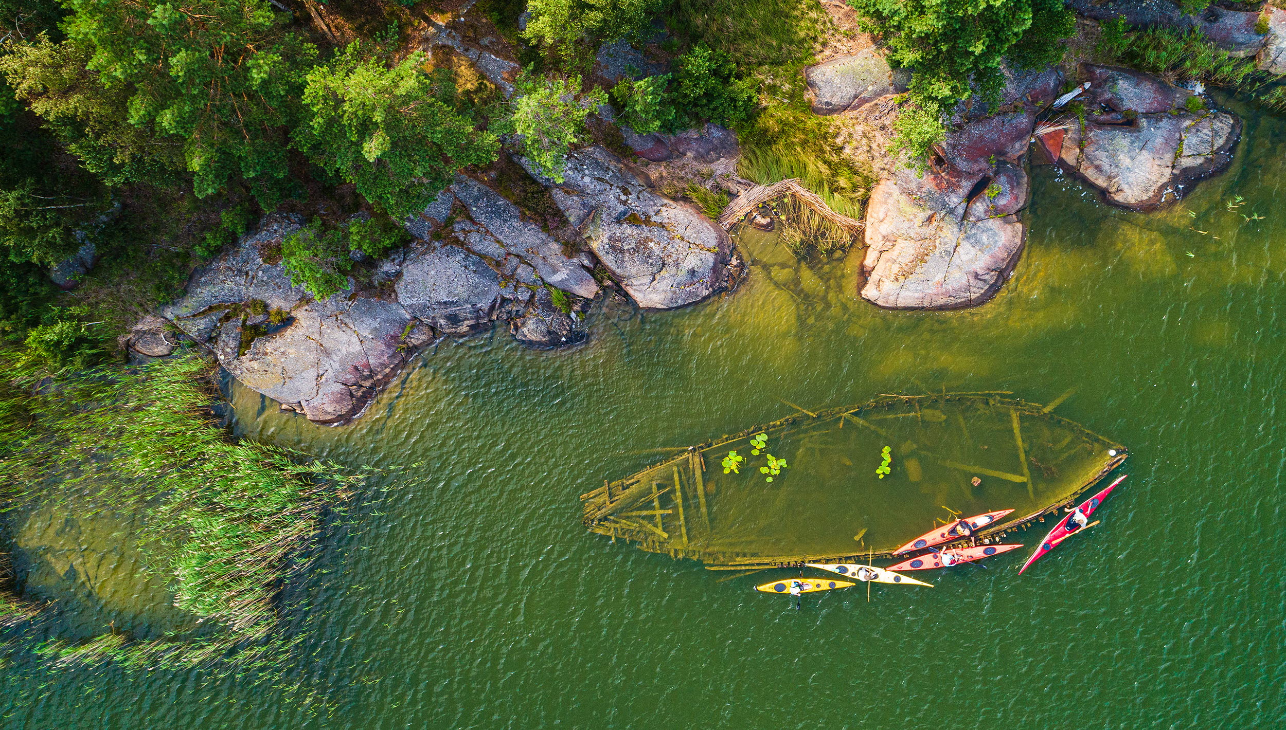A wreck lying near land in the water. It can be seen from above.
