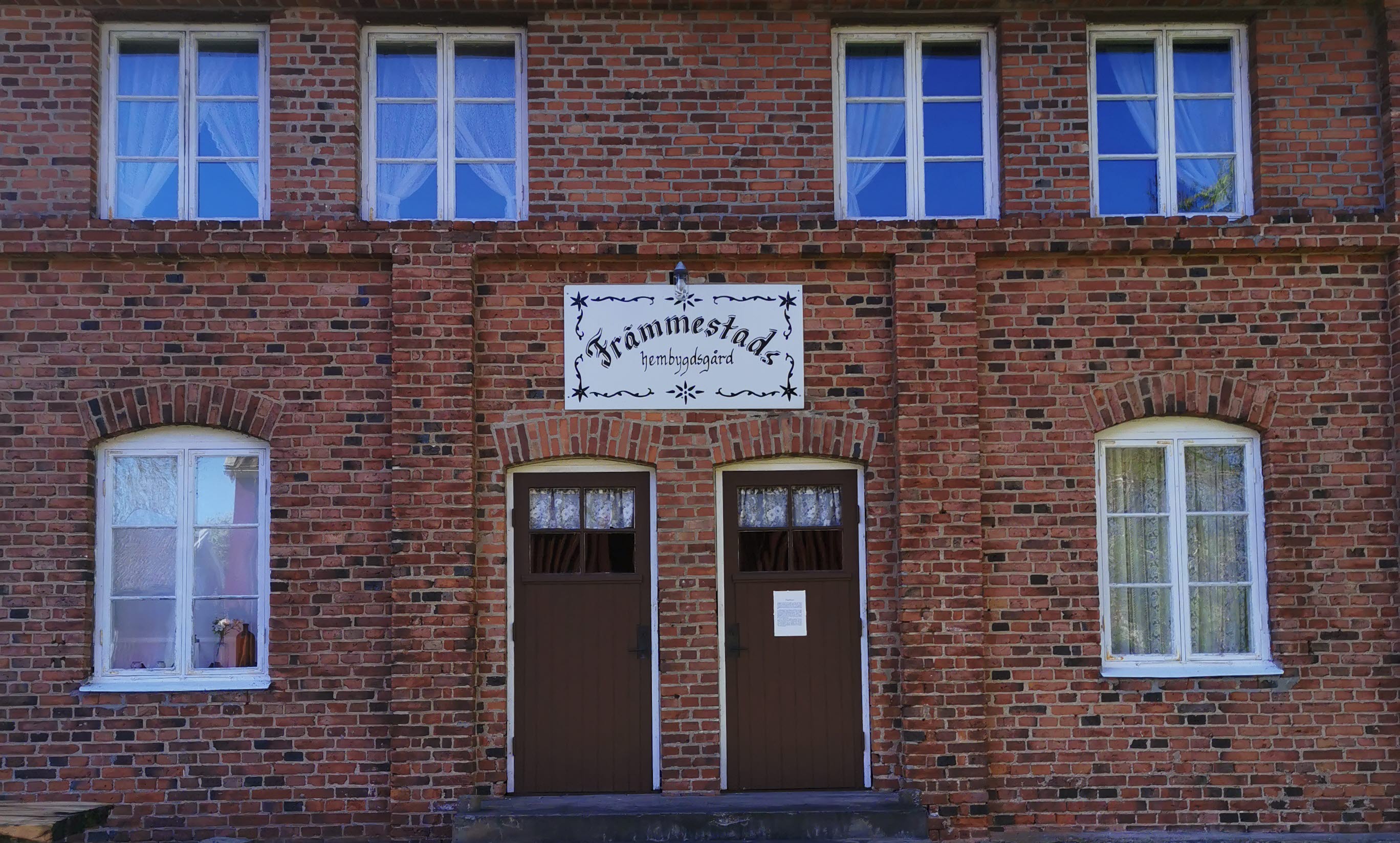 En fasad på en tegelbyggnad med höga fönster och två bruna dörrar.