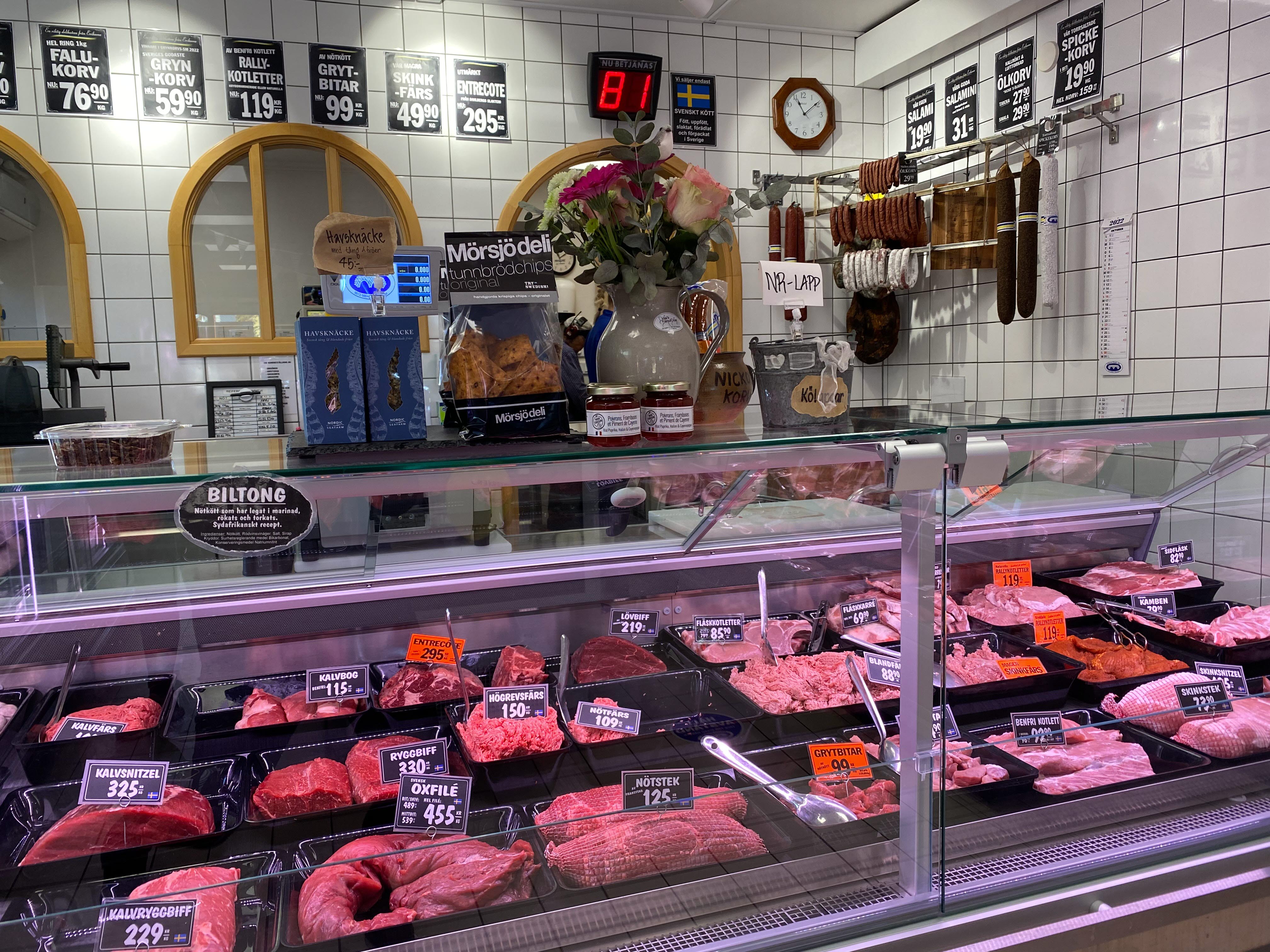 Inifrån ett butik som säljer kött så en disk med köttprodukter och vit kaklad vägg bakom. 