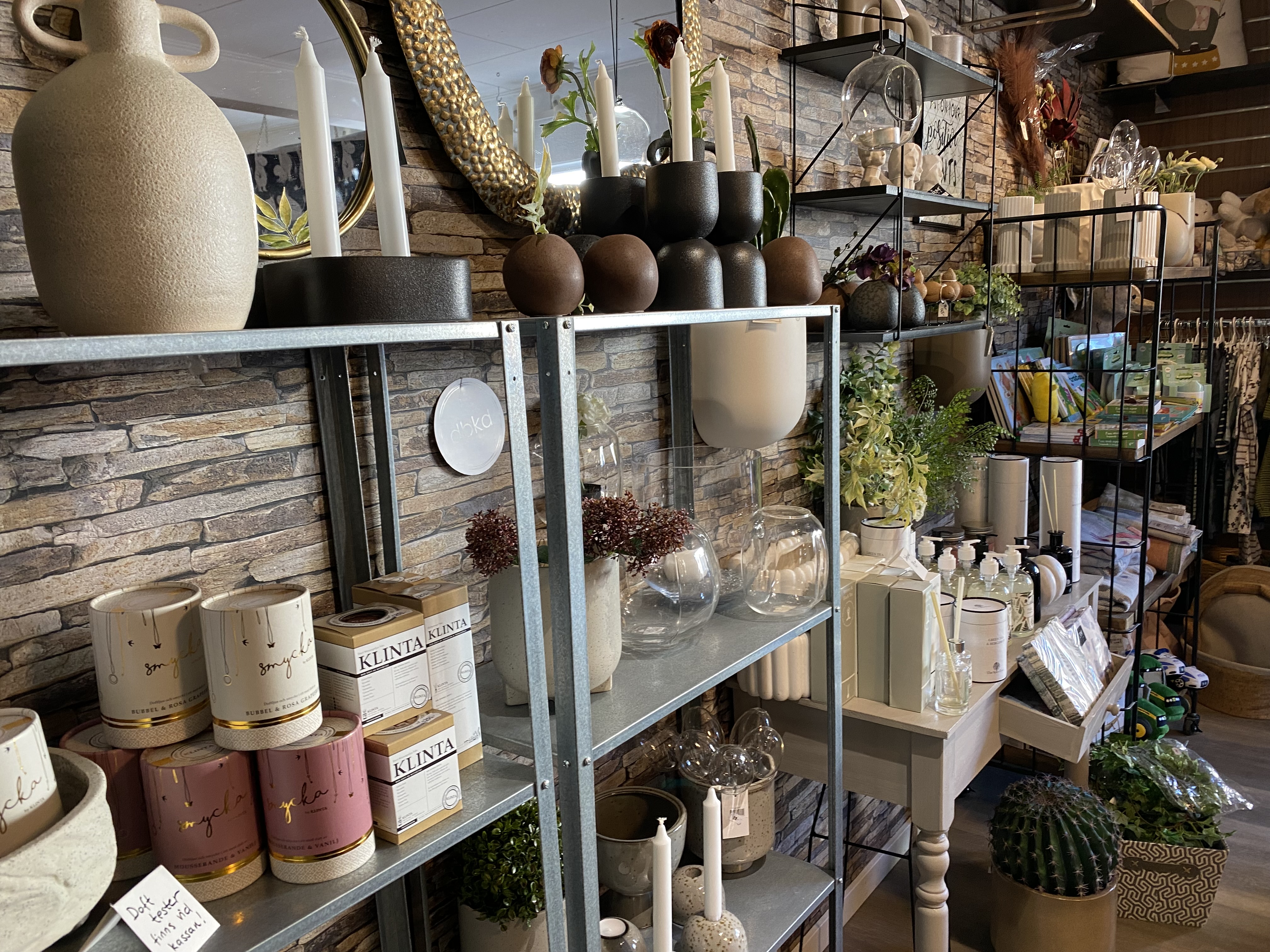 Inredning som står på hylla. Ljusstakar, krukor och någon blomma. 