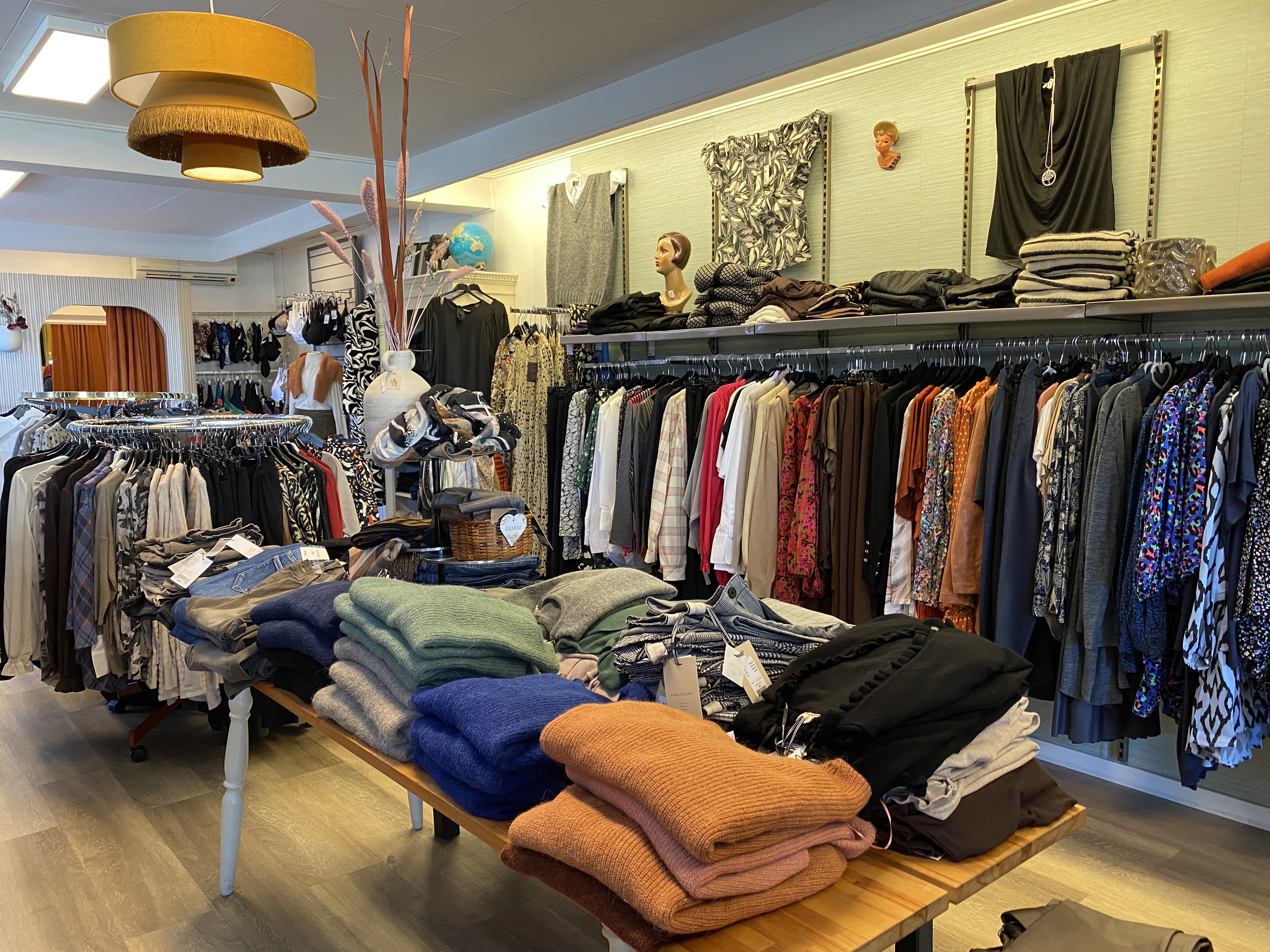 Massor med kläder i en klädbutik som hänger på en ställning och kläder som ligger i på ett bord. Många olika färger. 