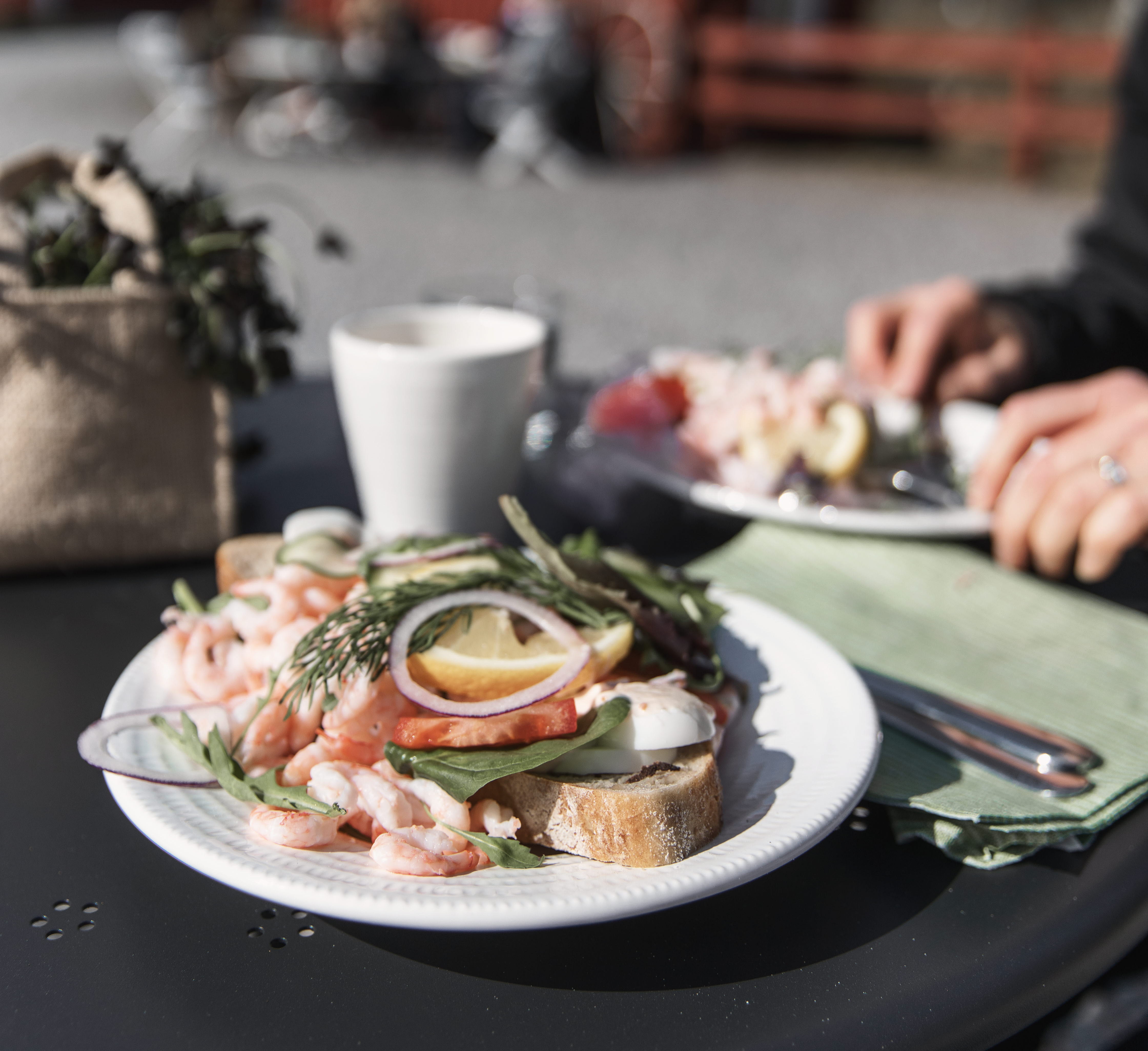 Ett bord utomhus med en tallrik med en smörgås med räkor på