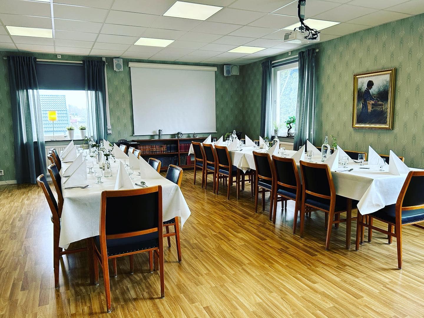 Inne i en restaurang. Gröna väggar, vita dukar på långbord.