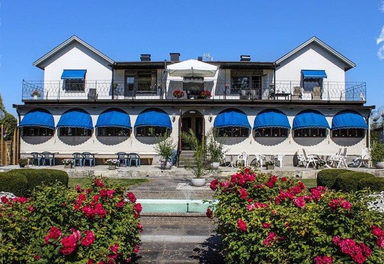 Ett vitt hus med blåa markiser. Rosa rosor i förgrunden. 