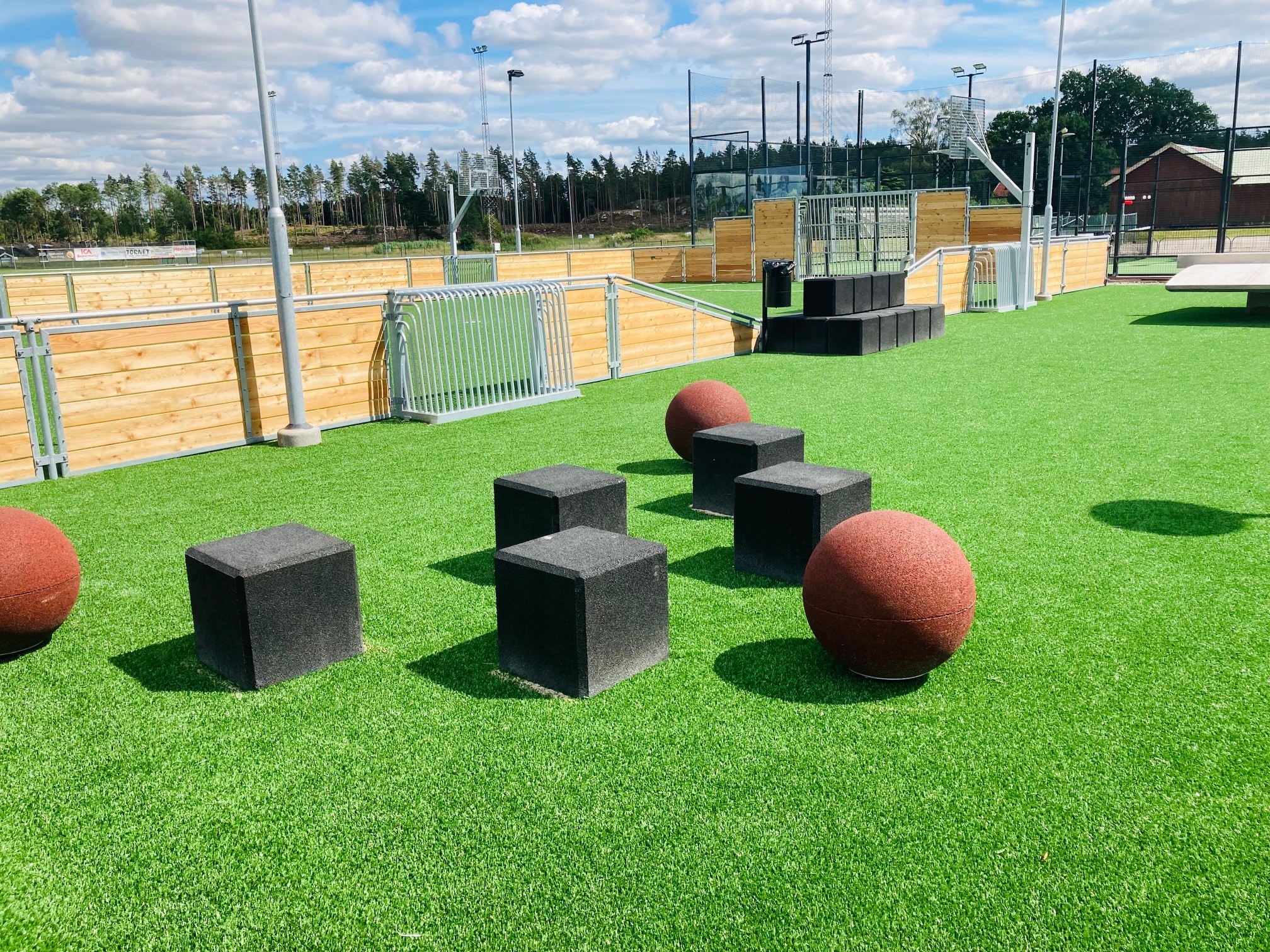 Grönt konstgräs med svarta fyrkanter som pallar på och röda bollar. 