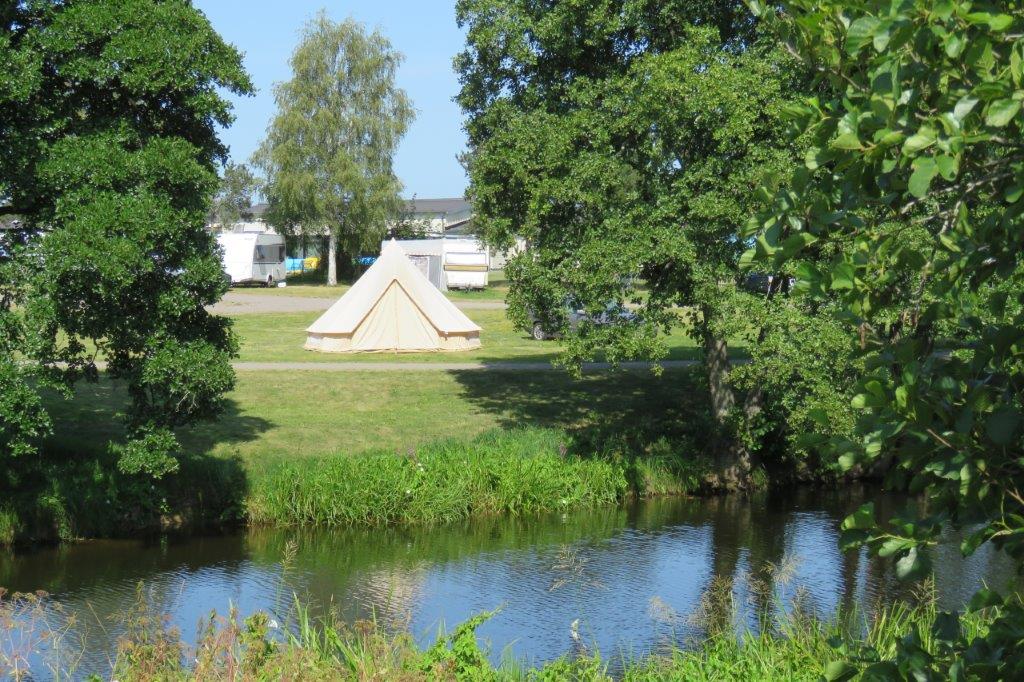 Ett tält som står på en gräsyta med en å framför