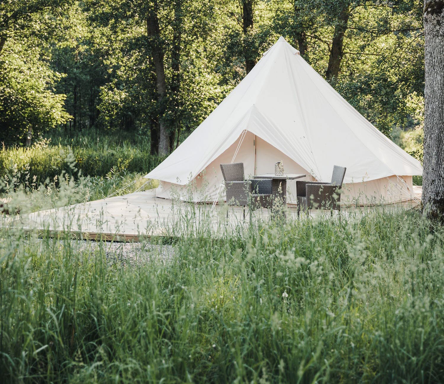 The exterior of a white glamping tent with a trolley outside. Trees and green.
