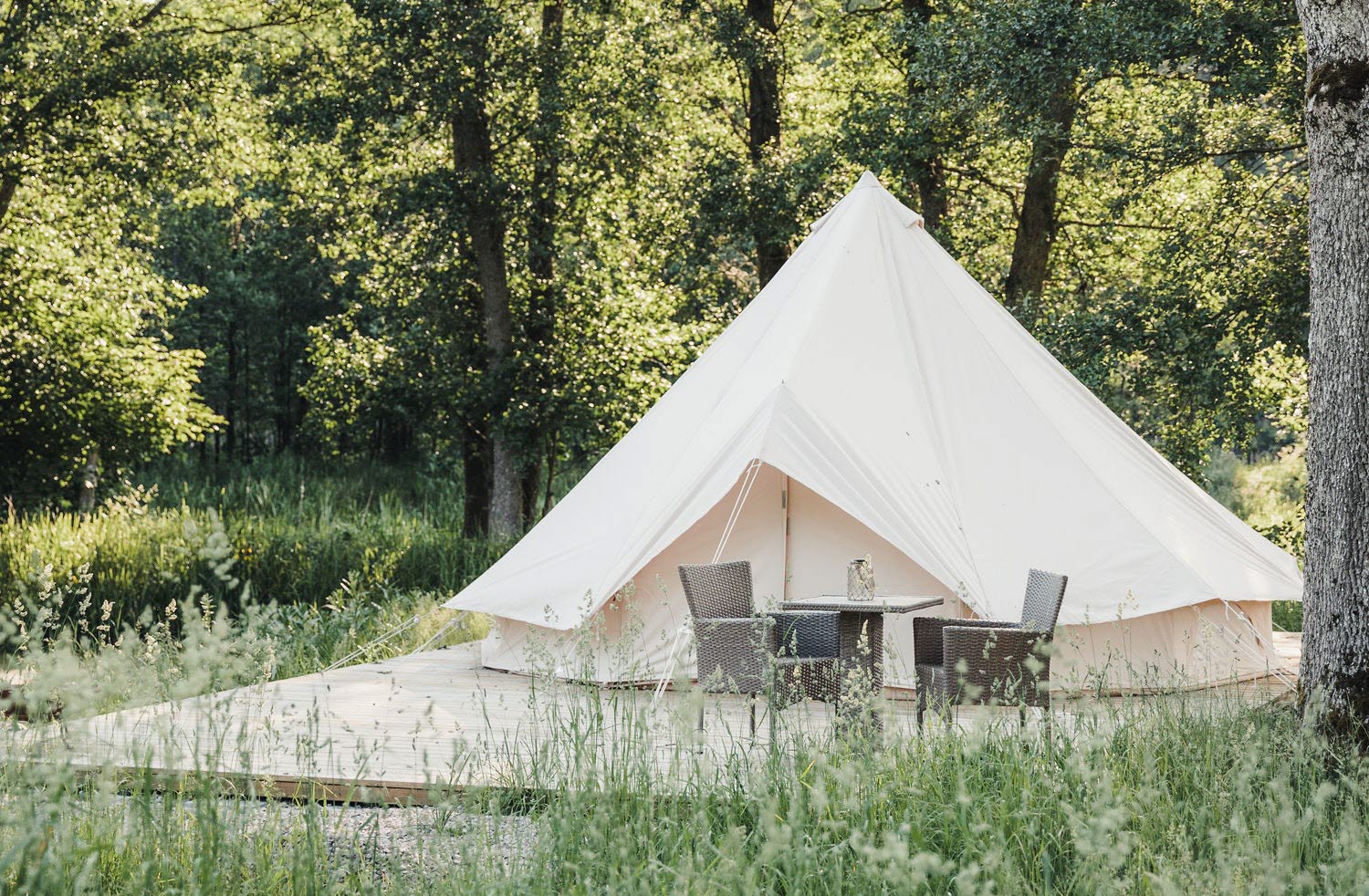 Utsidan på ett vitt glampingtält med en trall utanför. Träd och grönt. 